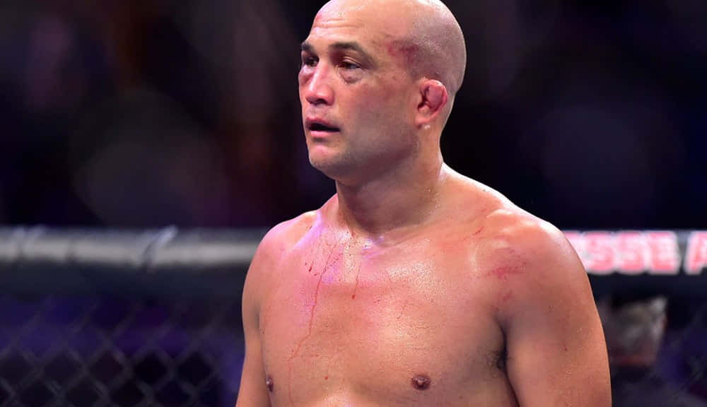 UFC 桌布 壁紙 — 一名渾身是血、筋疲力竭的混合武術選手在八角籠中，經過一場殘酷的比賽，汗水與傷口在明亮燈光下閃爍。