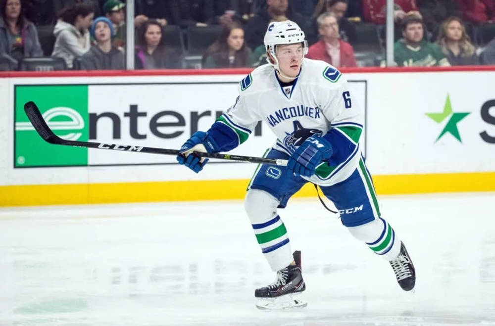 運動 桌布 壁紙 — 一名溫哥華加人隊（Vancouver Canucks）冰球運動員身穿白色、藍色和綠色球衣，在比賽中持球桿在冰上激烈滑行。
