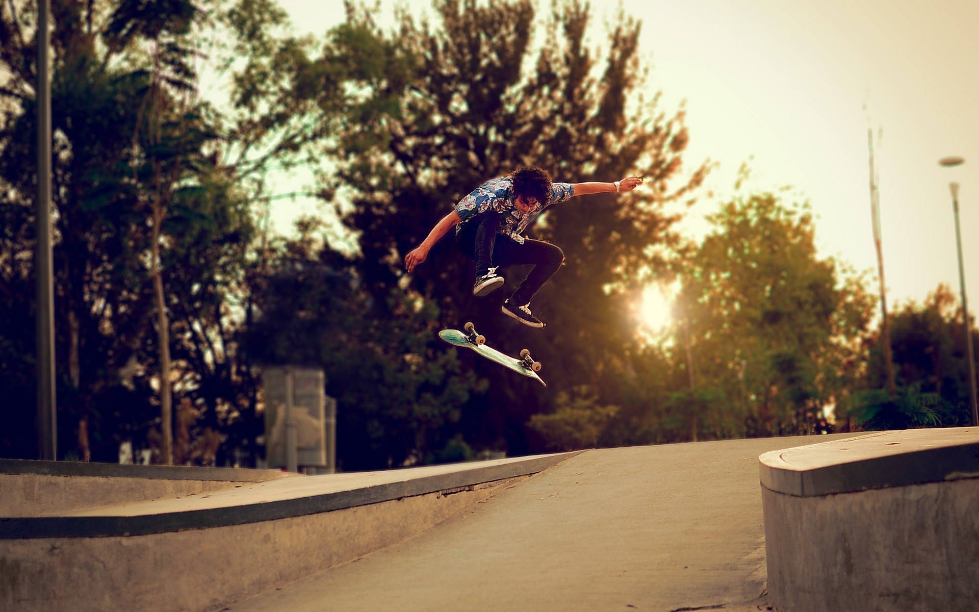 Skater Boy 桌布 壁紙 — 一名滑板手在半空中，在日落時分於混凝土坡道上表演技巧，背景有樹木。
