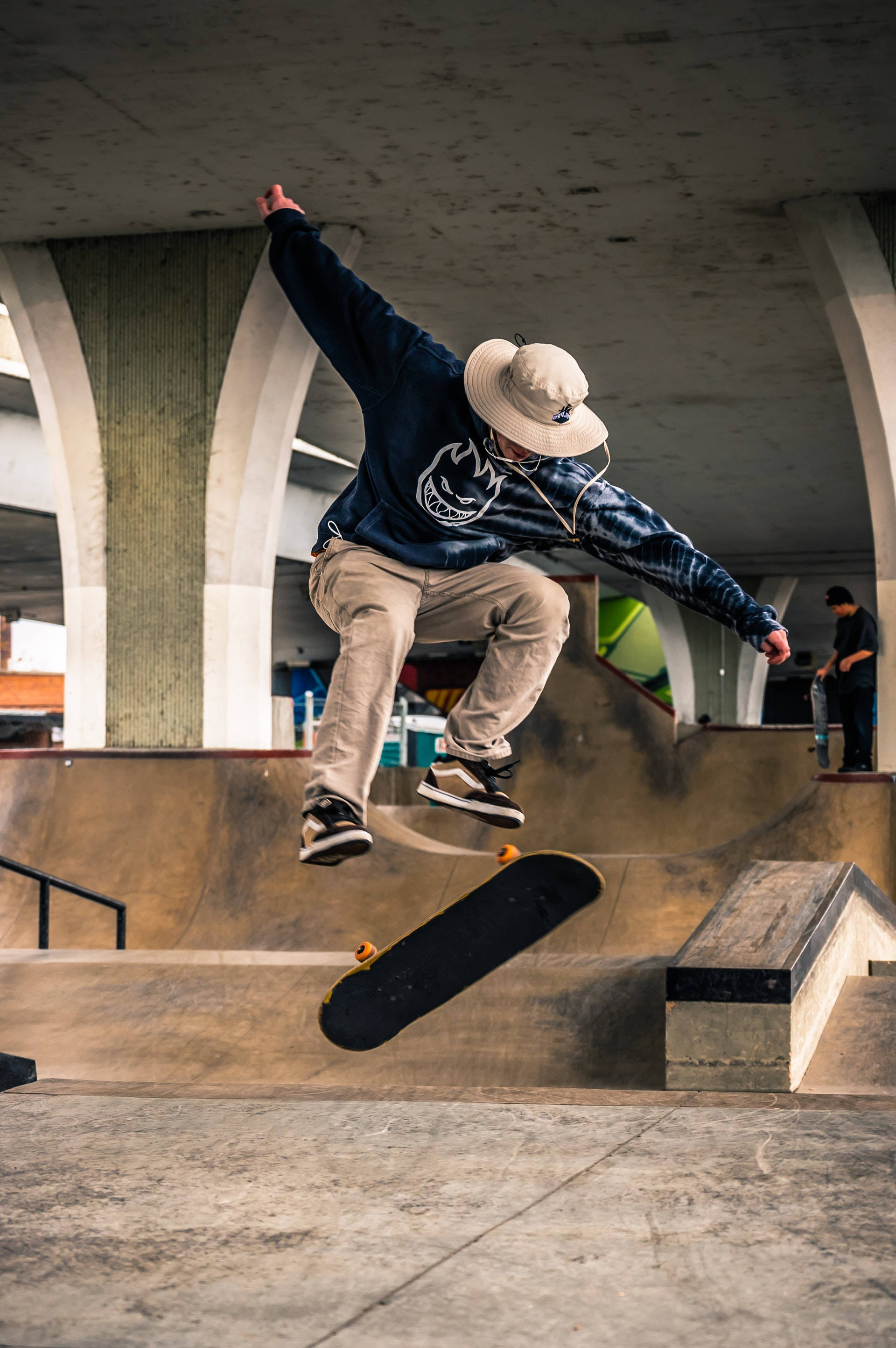 Skater Boy 桌布 壁紙 — 一名滑板手在半空中，於混凝土天橋下表演花式，下方有城市斜坡。