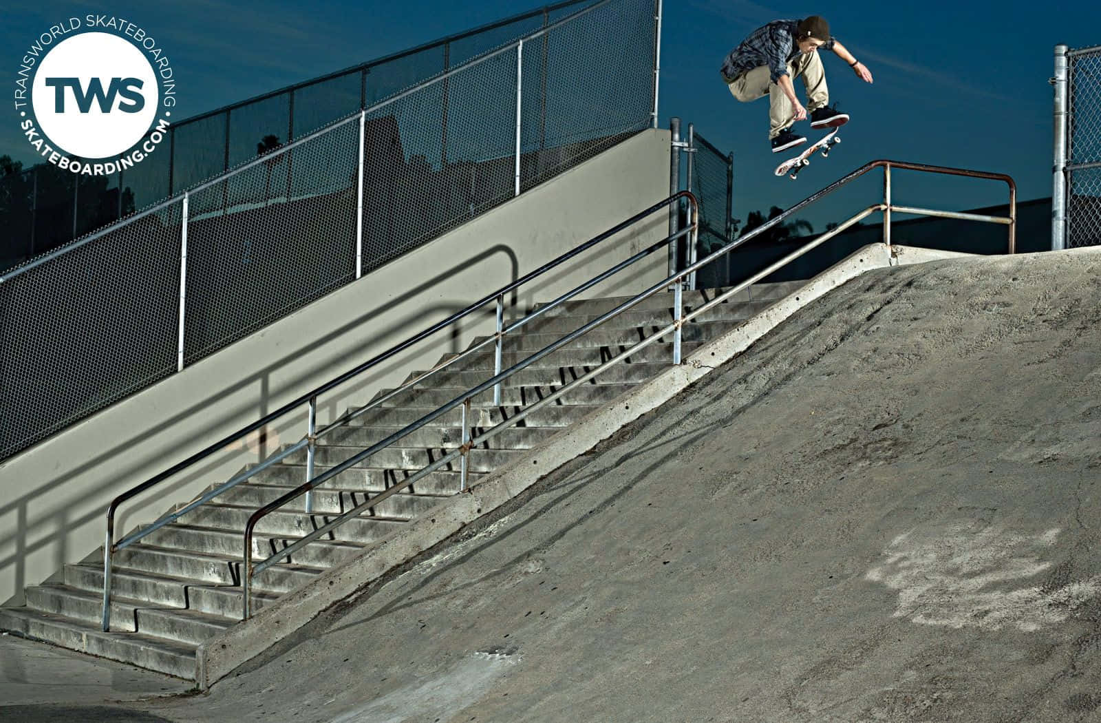 skate 桌布 壁紙 — 一名滑板手在半空中，於混凝土樓梯上表演技巧，背景是晴朗的藍天。