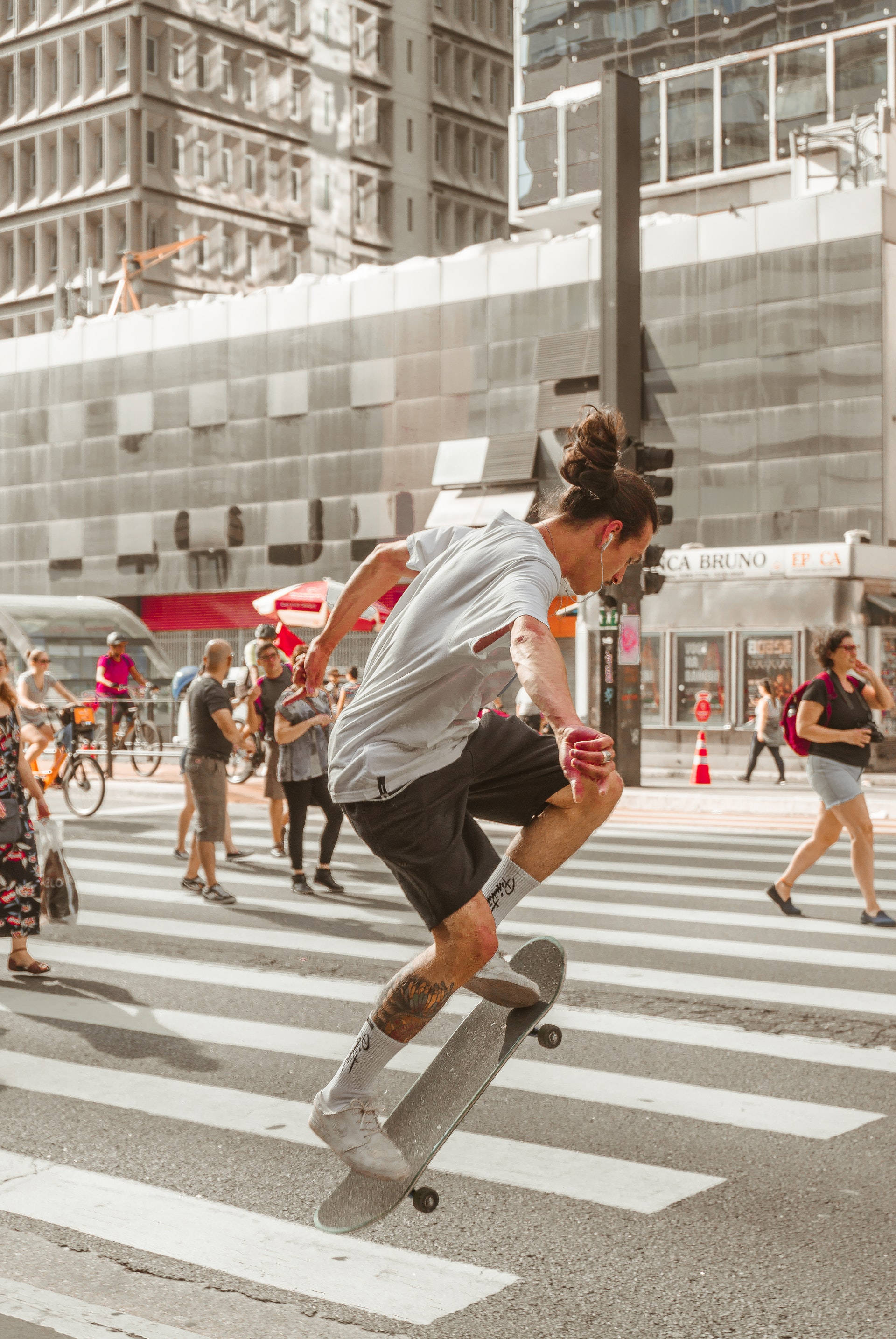 Skater Boy 桌布 壁紙 — 一名滑板手在半空中，於繁忙的城市行人穿越道上表演花式，背景有行人和現代建築物。