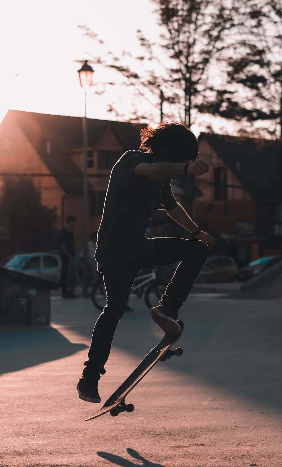 skateboarding 桌布 壁紙 — 一名滑板手在半空中，於陽光明媚的街道上，在黃金時刻的溫暖逆光下表演技巧。