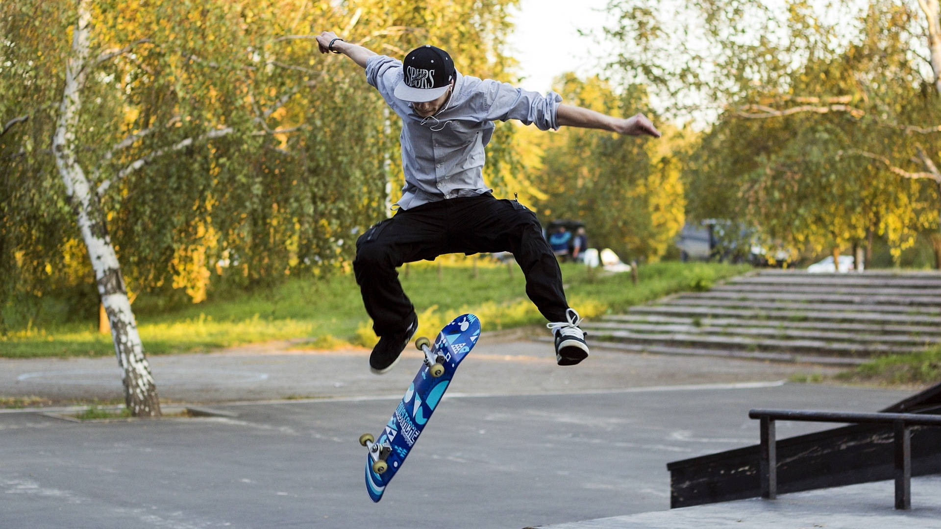 Skater Boy 桌布 壁紙 — 一名滑板手在半空中伸展雙臂表演技巧，背景是秋樹和混凝土階梯。