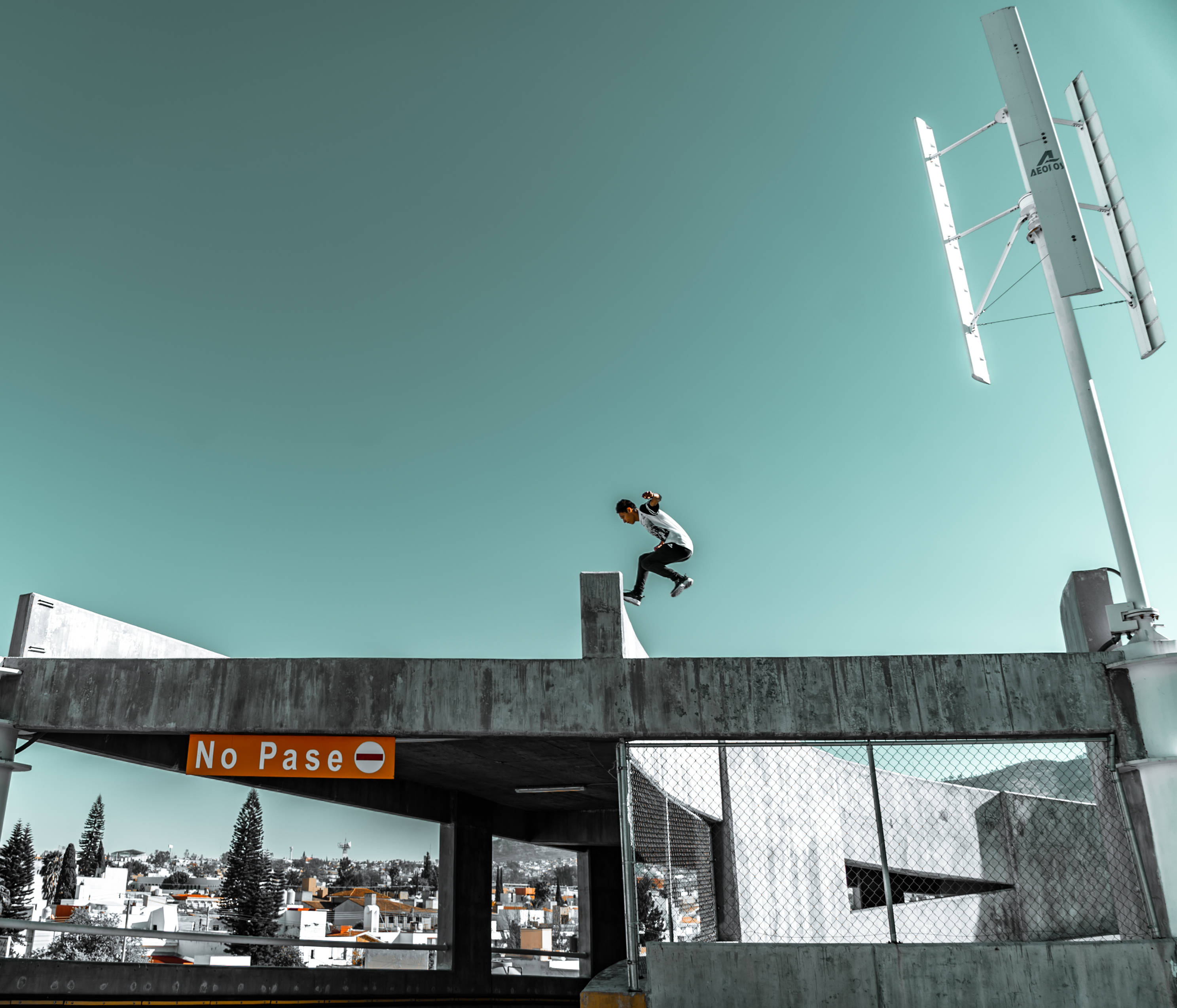 Parkour 桌布 壁紙 — 一名滑板手在半空中越過混凝土障礙物，下方是城市景觀，上方是清澈的藍綠色天空。