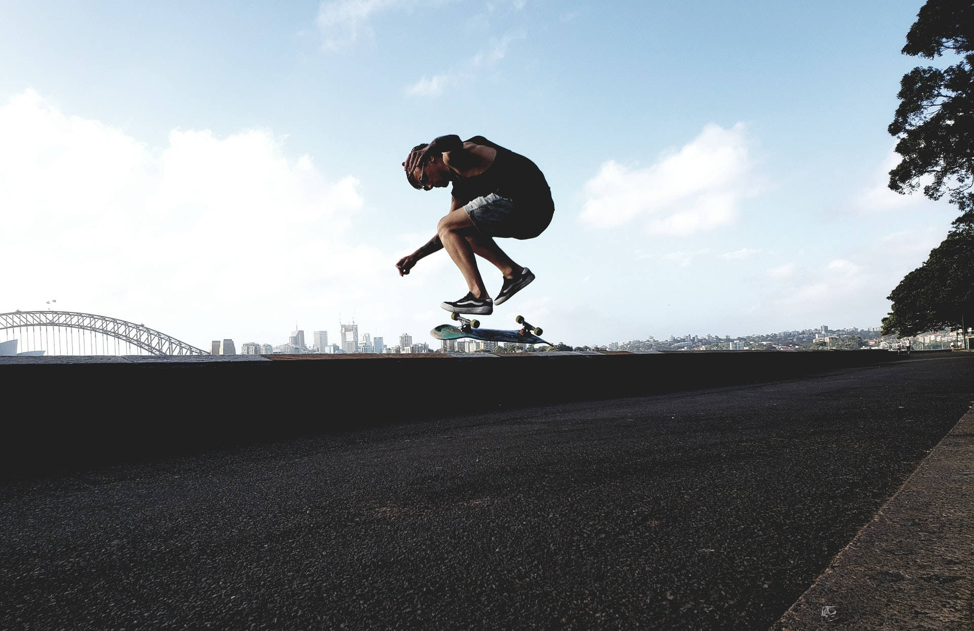 Skater Boy 桌布 壁紙 — 一名滑板手在半空中越過邊緣表演技巧，背景是雪梨港灣大橋和城市天際線。