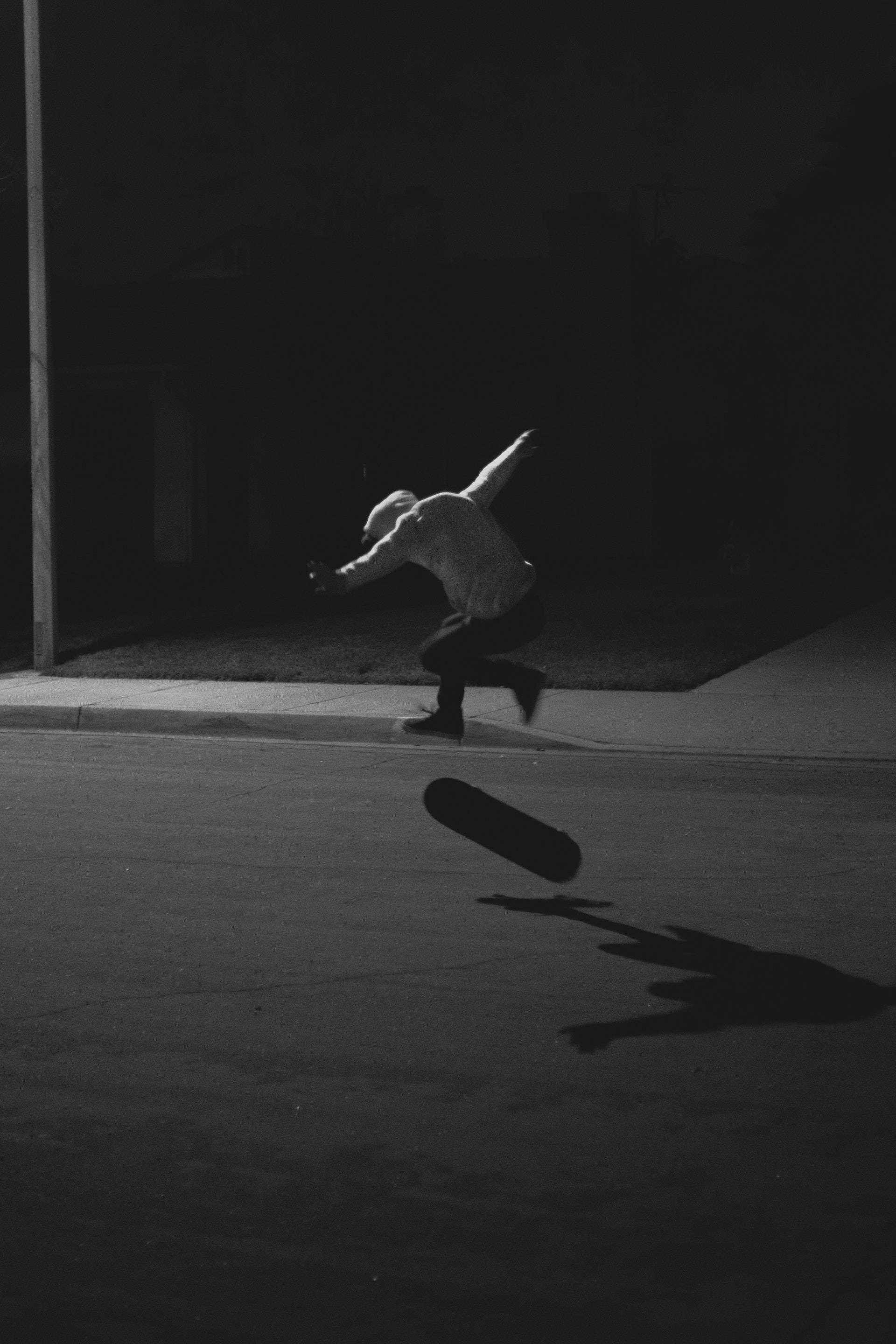 Skater Boy 桌布 壁紙 — 一名滑板手在夜間街燈下凌空表演花式，在人行道上留下長長的影子。