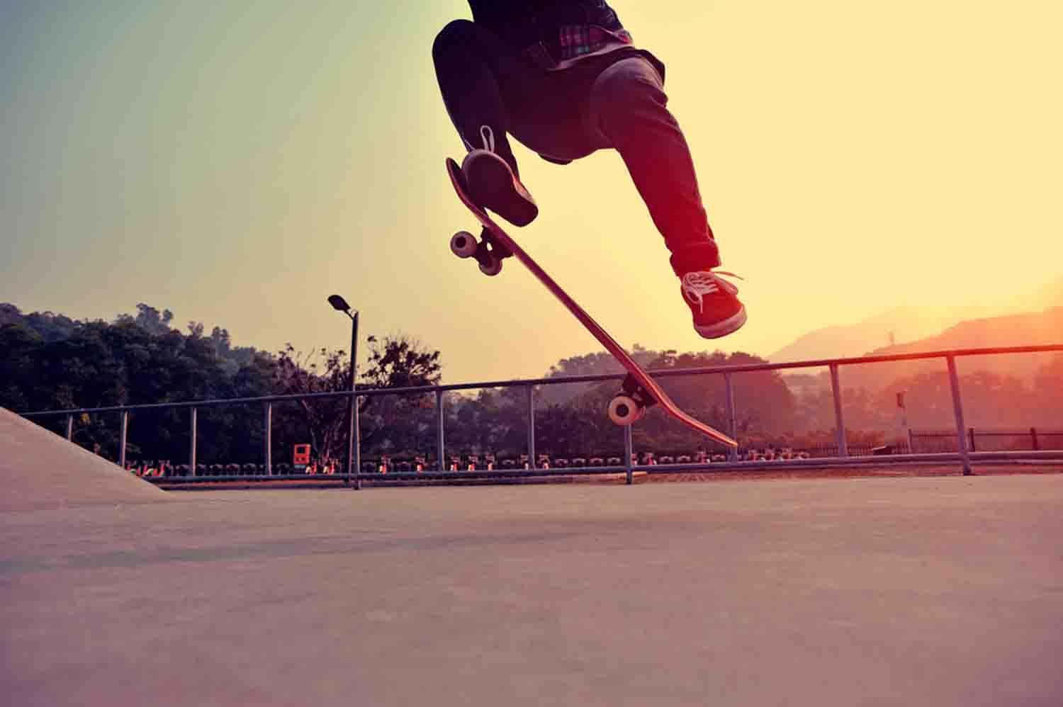 skateboarding 桌布 壁紙 — 一名滑板手在日落時分於混凝土滑板公園上空，在溫暖的金色光線中表演花式。