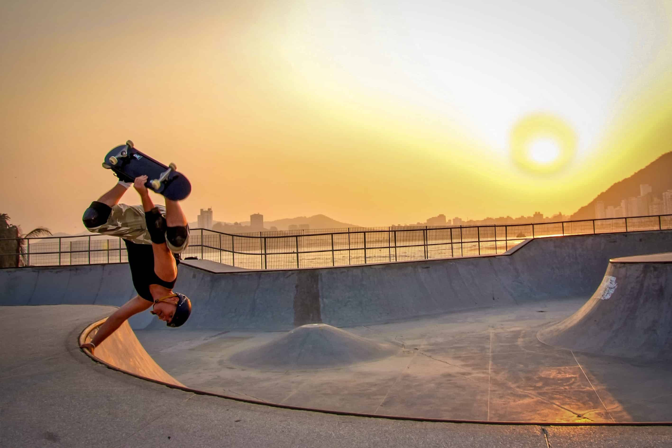 Skater Boy 桌布 壁紙 — 一名滑板手在日落時分於混凝土滑板公園中，在橙紅色天空下表演倒轉技巧。