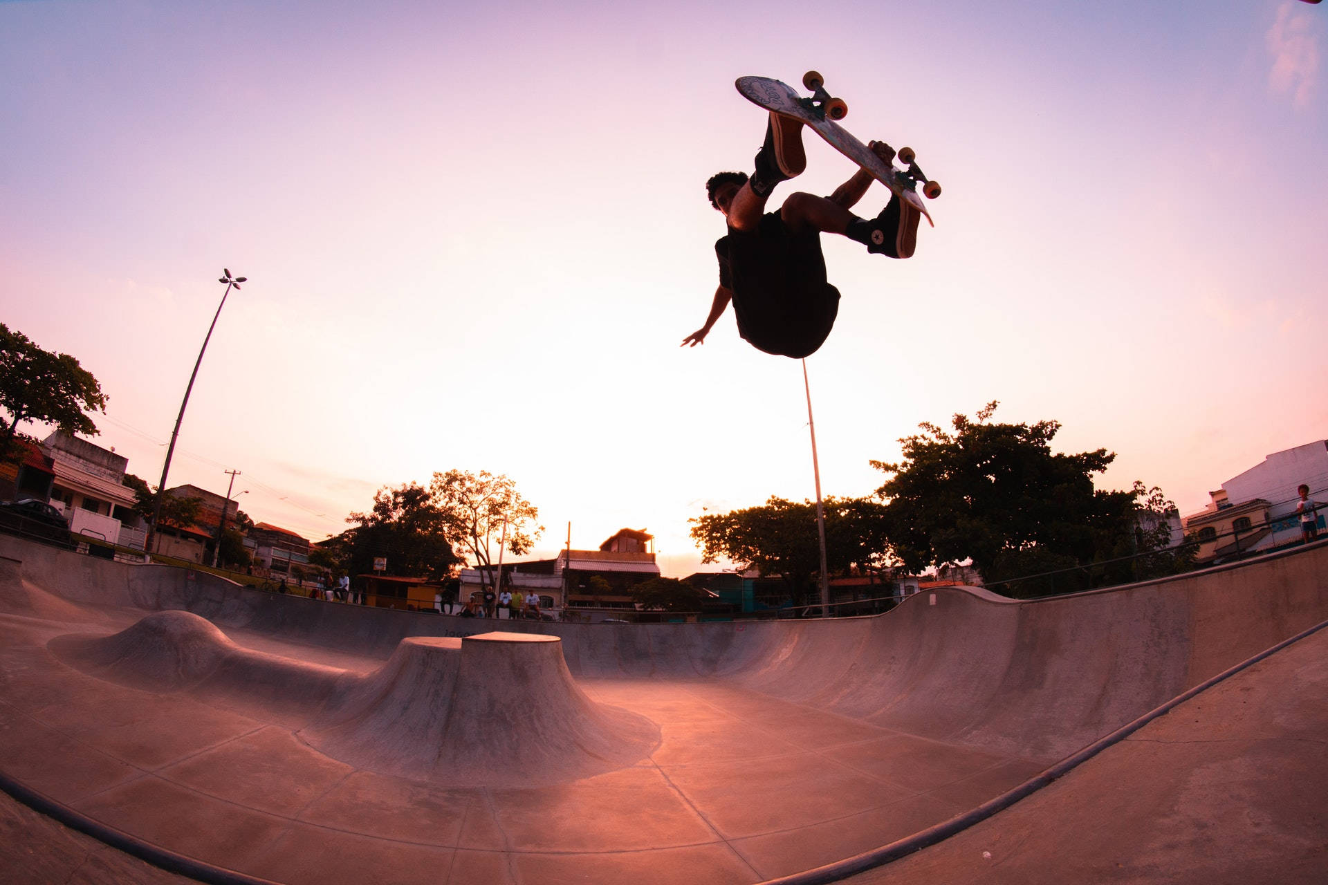 Skater Boy 桌布 壁紙 — 一名滑板手在日落時分於混凝土滑板公園中，在溫暖發光的光線下表演空中技巧。