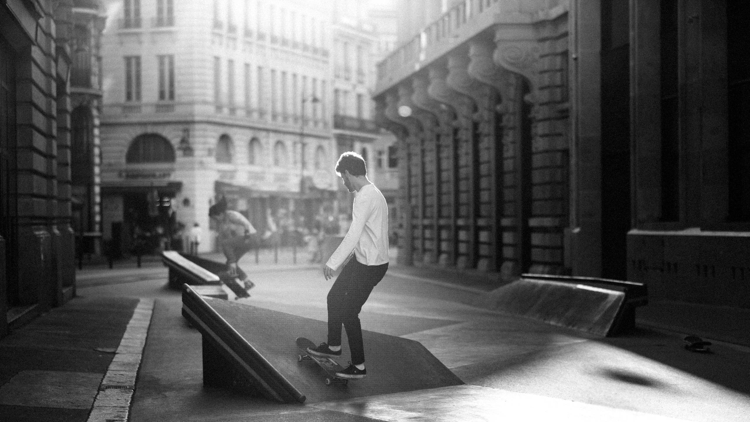 Skater Boy 桌布 壁紙 — 一名滑板手在歷史建築之間的陽光普照的城市小巷中，以黑白風格磨擦邊緣。