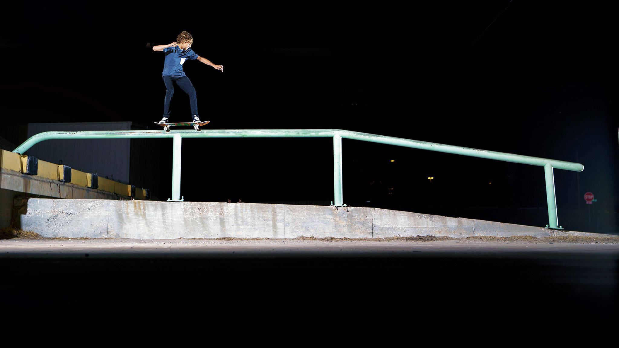 Skater Boy 桌布 壁紙 — 一名滑板手在漆黑的夜空下，於強烈燈光中熟練地平衡在發光的綠色欄杆上。