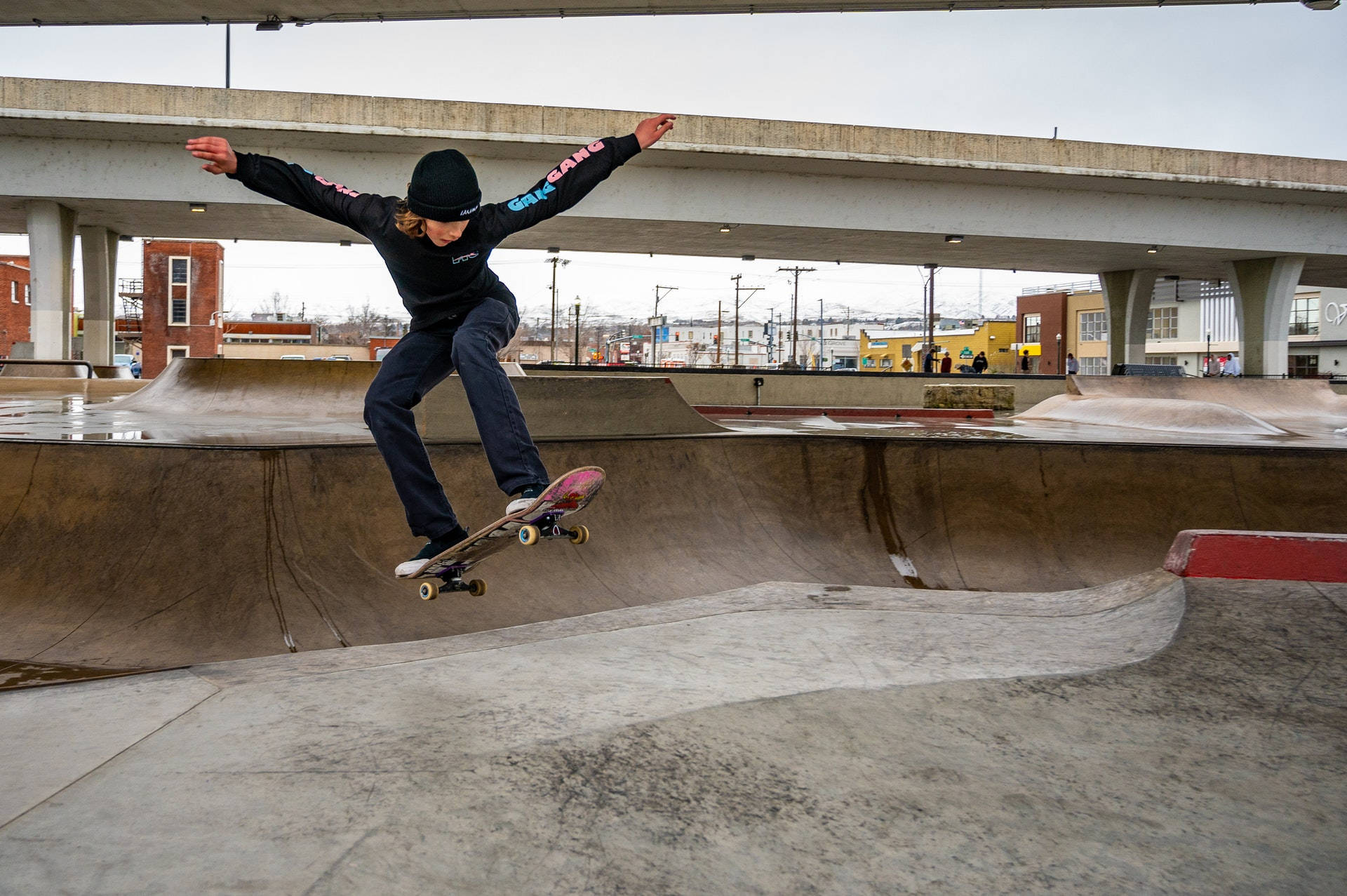 Skater Boy 桌布 壁紙 — 一名滑板手在陰天於天橋下的混凝土滑板公園上空表演技巧。
