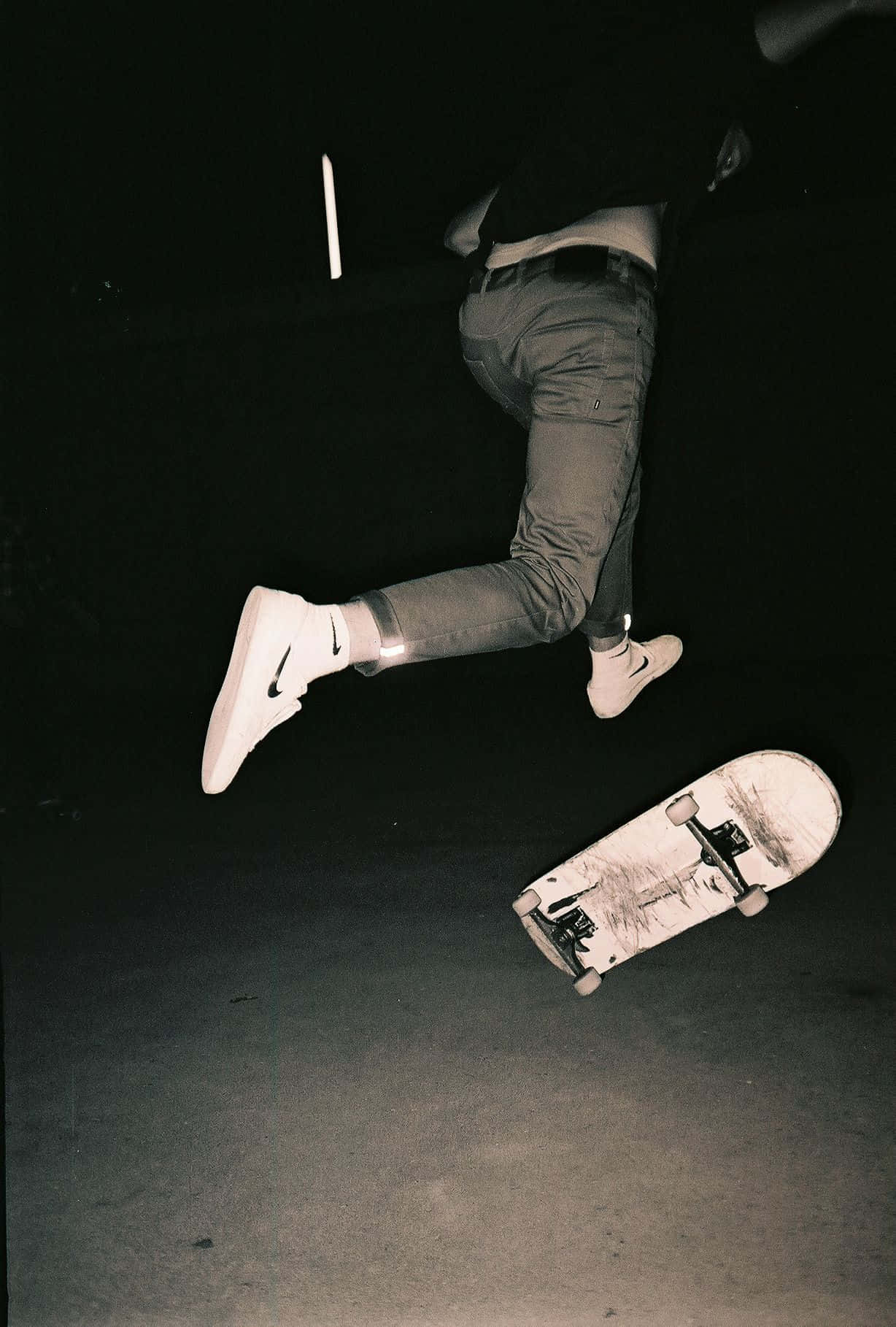 Retro Skateboard 桌布 壁紙 — 一名滑板手在黑暗夜間燈光下，於裂開的混凝土表面上方騰空，穿著白色運動鞋，下方有一塊翻轉的滑板。