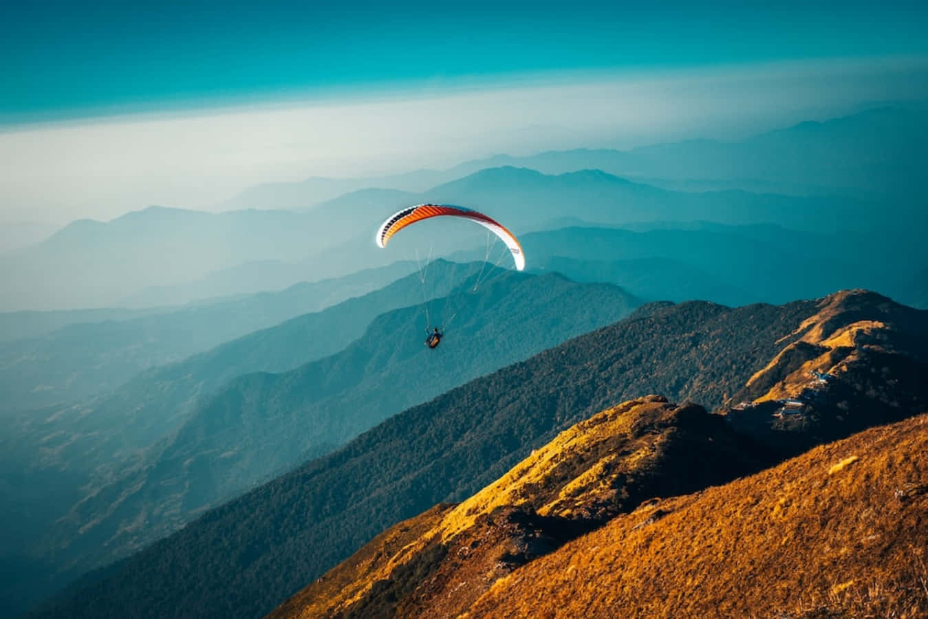 adventure 桌布 壁紙 — 一名滑翔傘運動員在清澈的藍天下翱翔於層層疊疊的山脊之上，金色的陽光照亮了前景的山坡。