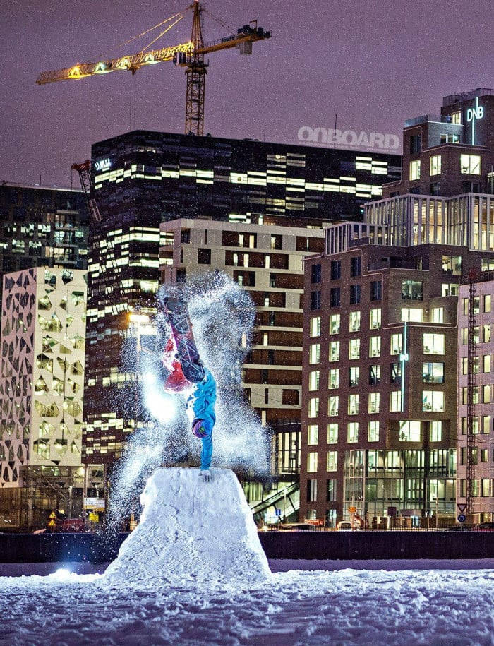 城市 桌布 壁紙 — 一名滑雪板手在夜間於雪堆上表演倒立技巧，背景是充滿活力的城市天際線。