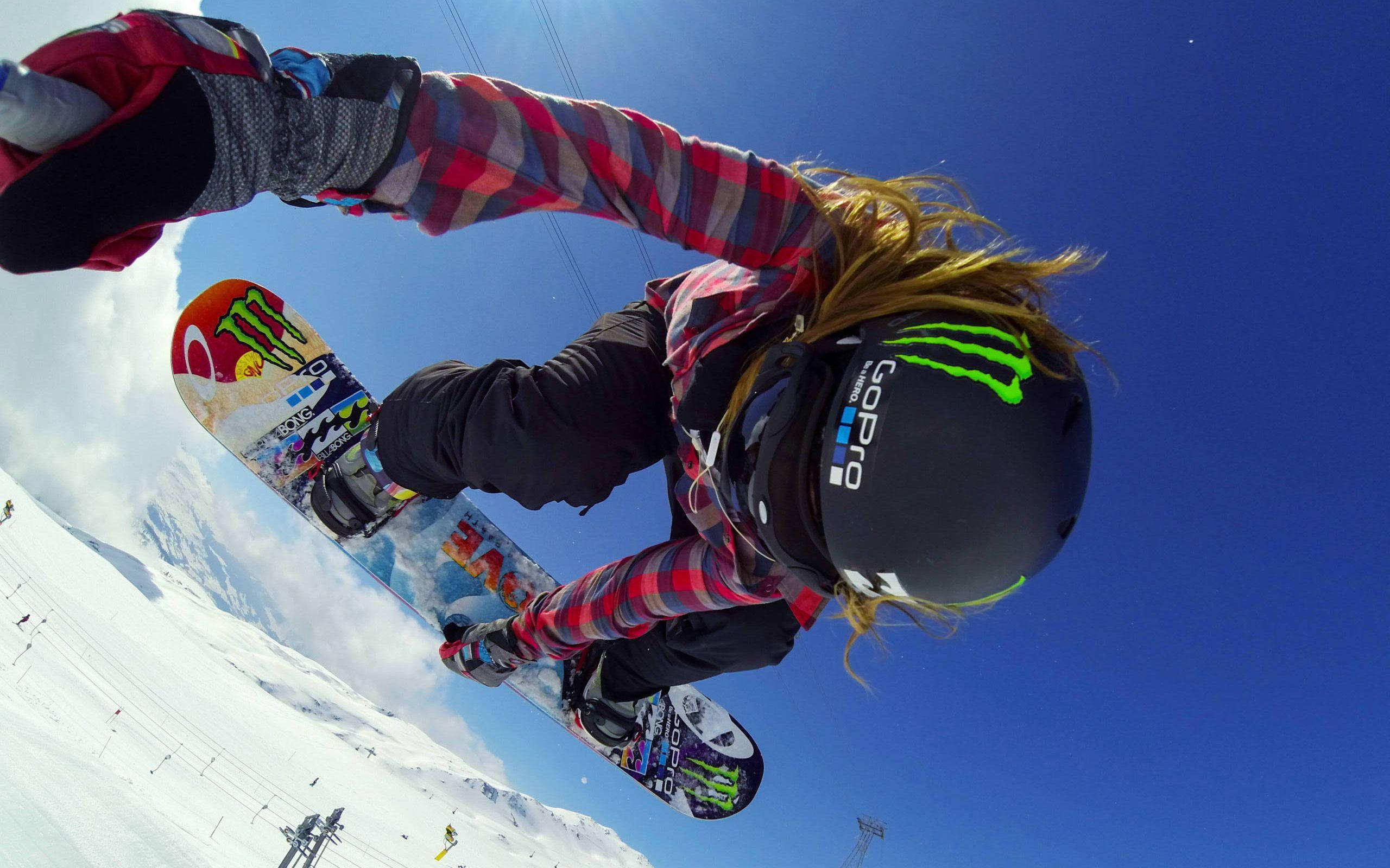 gopro 桌布 壁紙 — 一名滑雪板運動員在明亮的藍天下騰空，下方是白雪覆蓋的山脈。