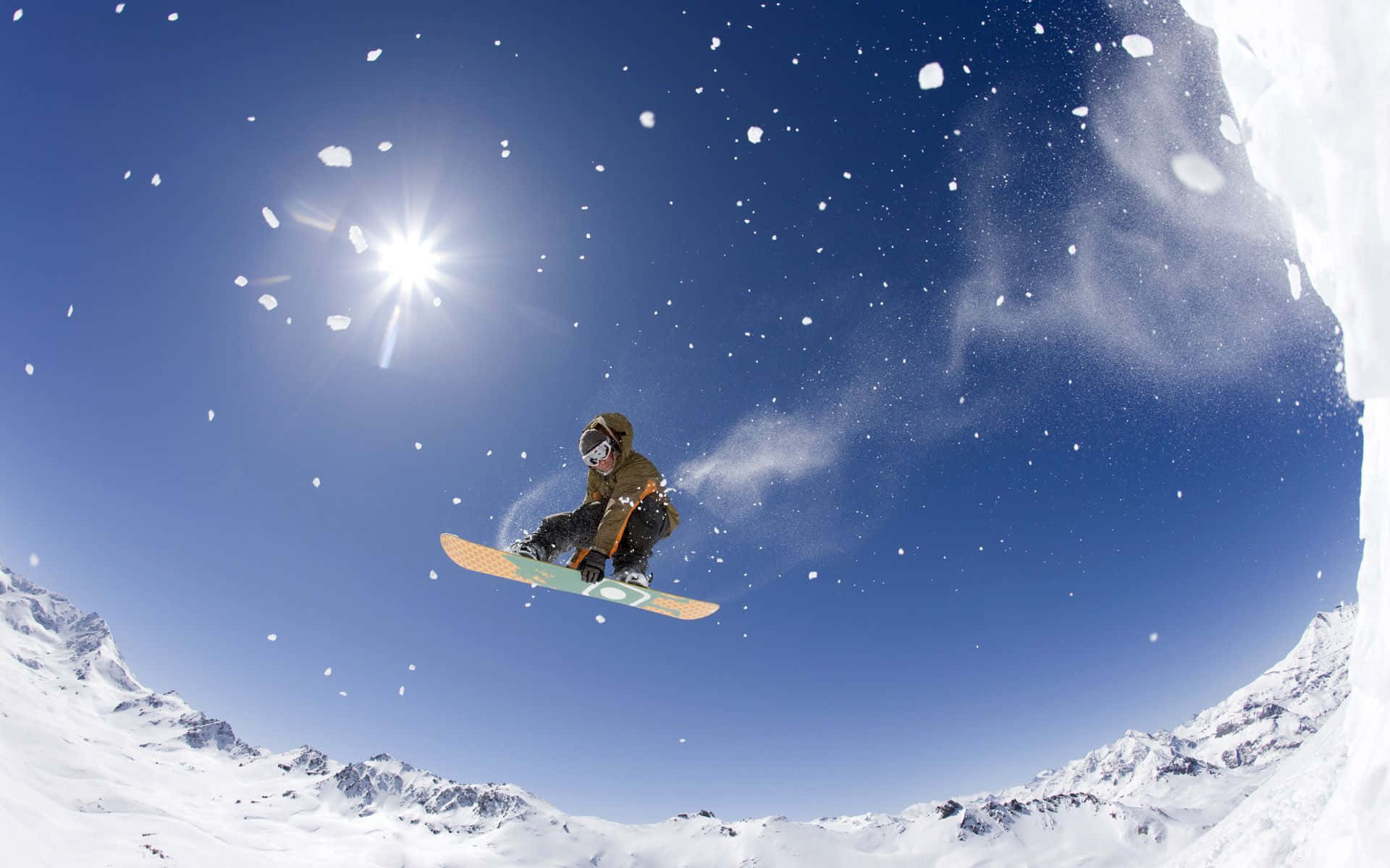 Winter Sports 桌布 壁紙 — 一名滑雪板運動員在晴朗的冬日空氣中翱翔，背景是燦爛的藍天，陽光閃耀，雪花在周圍旋轉。
