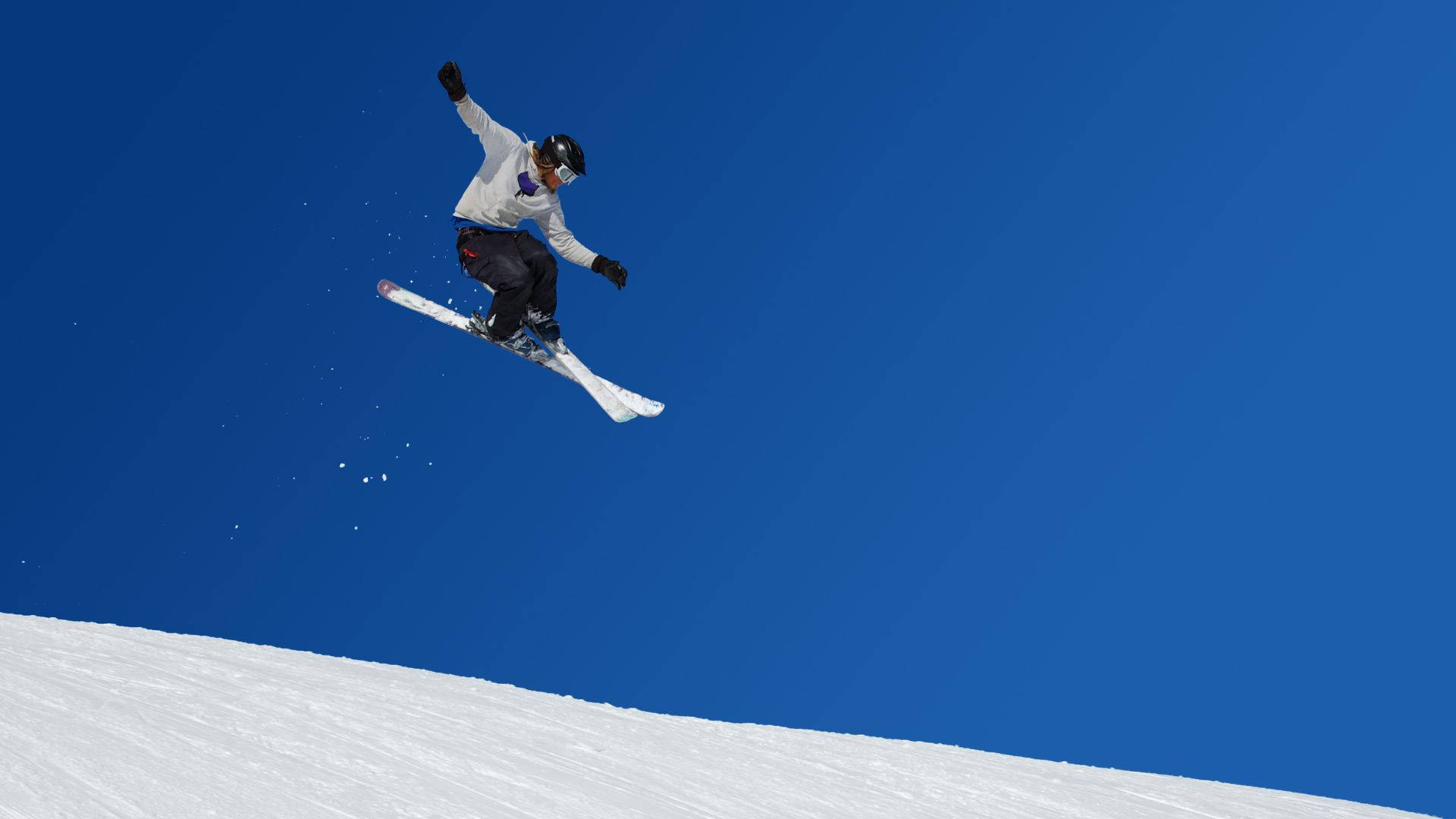 冬天 桌布 壁紙 — 一名滑雪板運動員在晴朗的藍天中飛翔，越過白雪覆蓋的斜坡，高舉雙臂慶祝勝利。