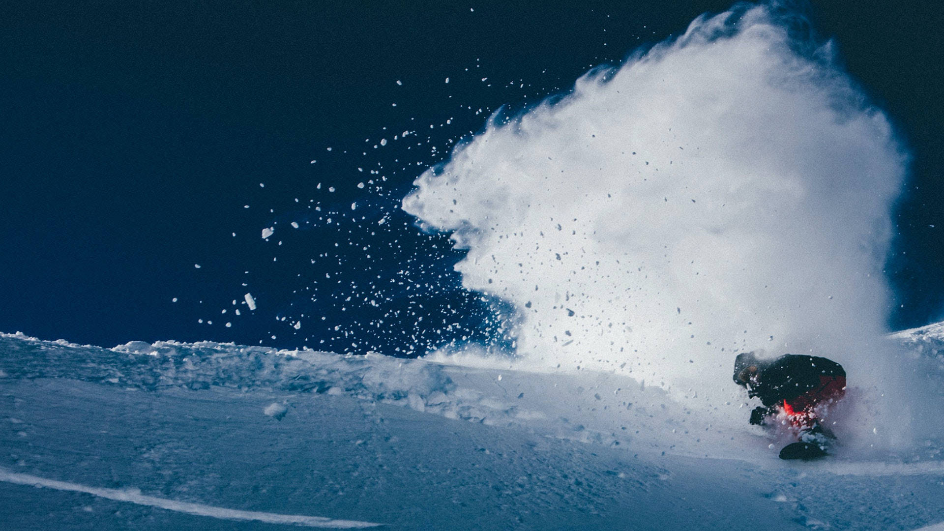 Snowboarding 桌布 壁紙 — 一名滑雪板運動員在深粉雪中 carving，將大量白色雪花噴向清澈的藍天。