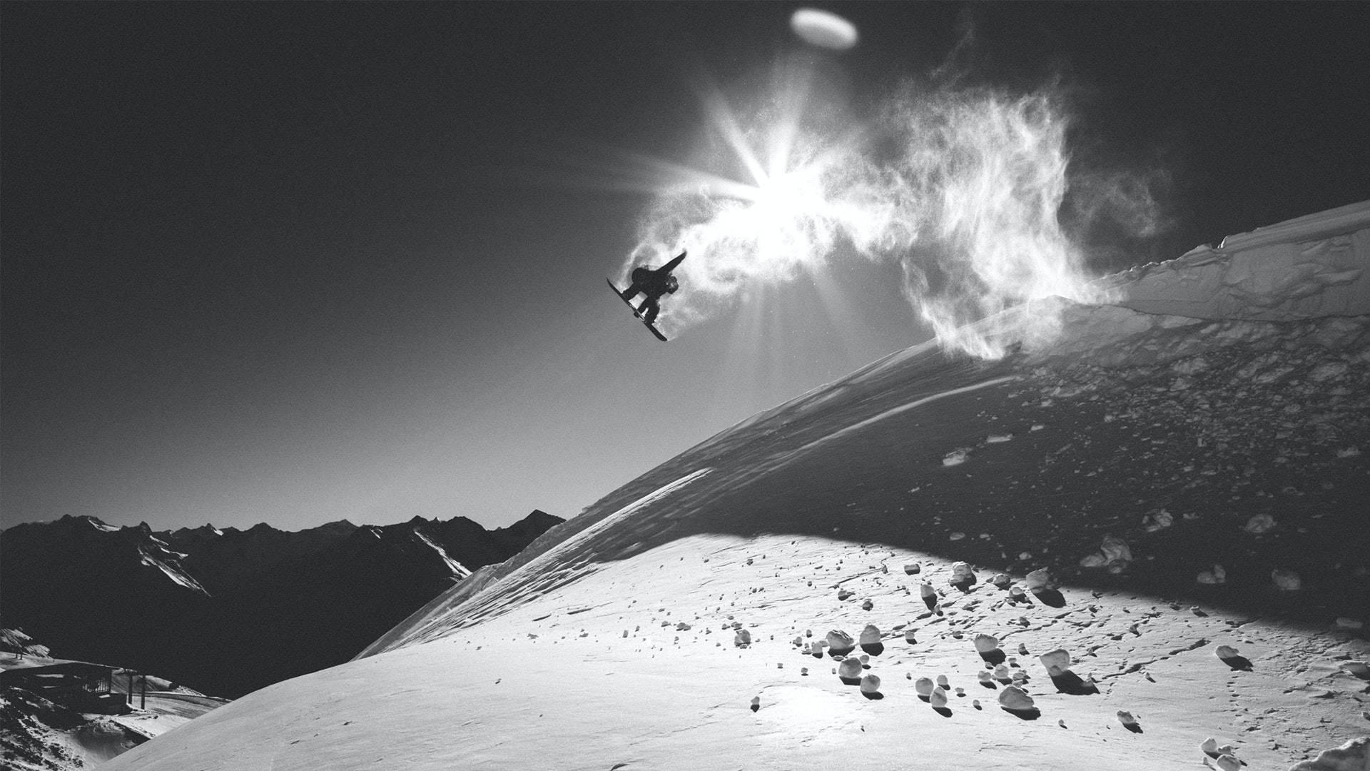 Snowboarding 桌布 壁紙 — 一名滑雪板運動員在白雪覆蓋的山坡上空飛翔，背後太陽閃耀。