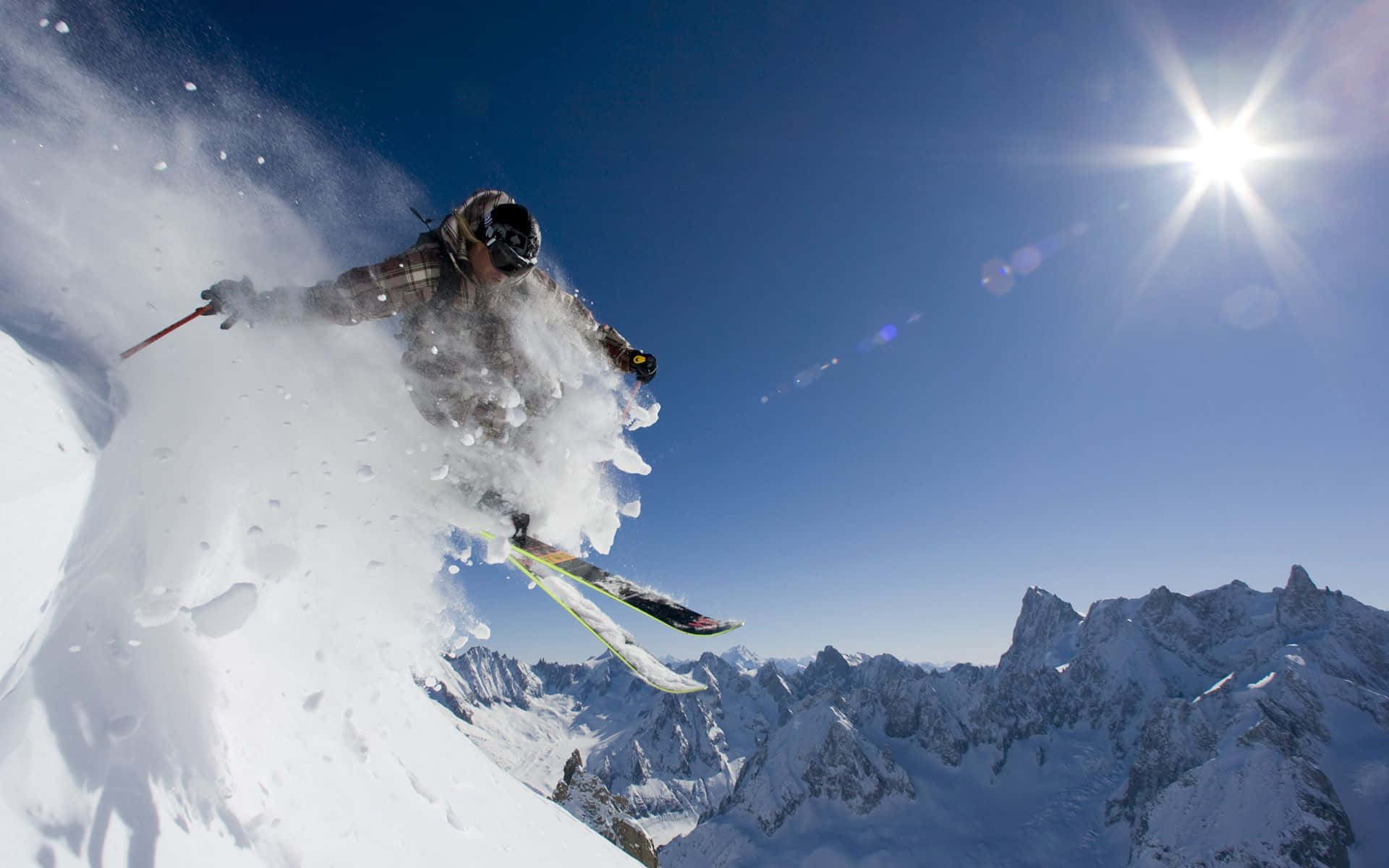 Winter Sports 桌布 壁紙 — 一名滑雪者在陽光普照的山坡上劃過新雪，將雪花濺向明亮的藍天。