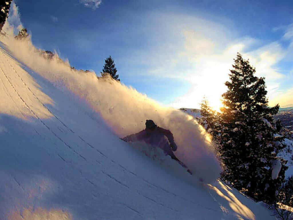Winter Sports 桌布 壁紙 — 一名滑雪者在雪坡上劃過新鮮的粉雪，金色的夕陽光芒灑滿整個場景。