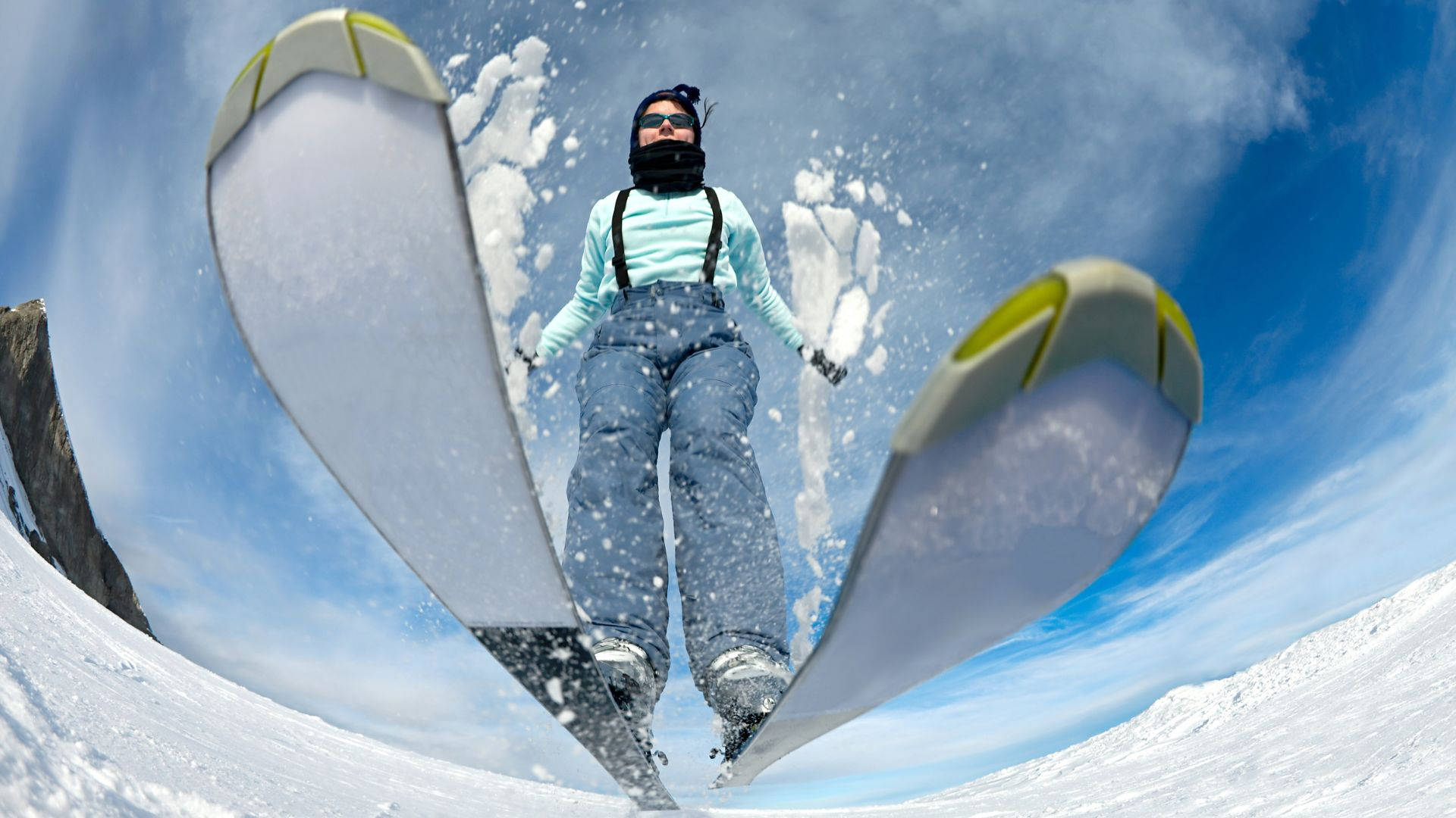 冬天 桌布 壁紙 — 一名滑雪者在雪坡上空翱翔，滑雪板向上傾斜，映襯著明亮的藍天。