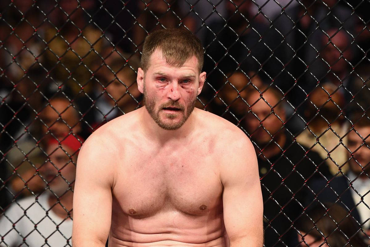 UFC 桌布 壁紙 — 一名滿臉傷痕、血跡斑斑的拳手疲憊地坐在籠內，背景是鐵絲網後模糊的人群。