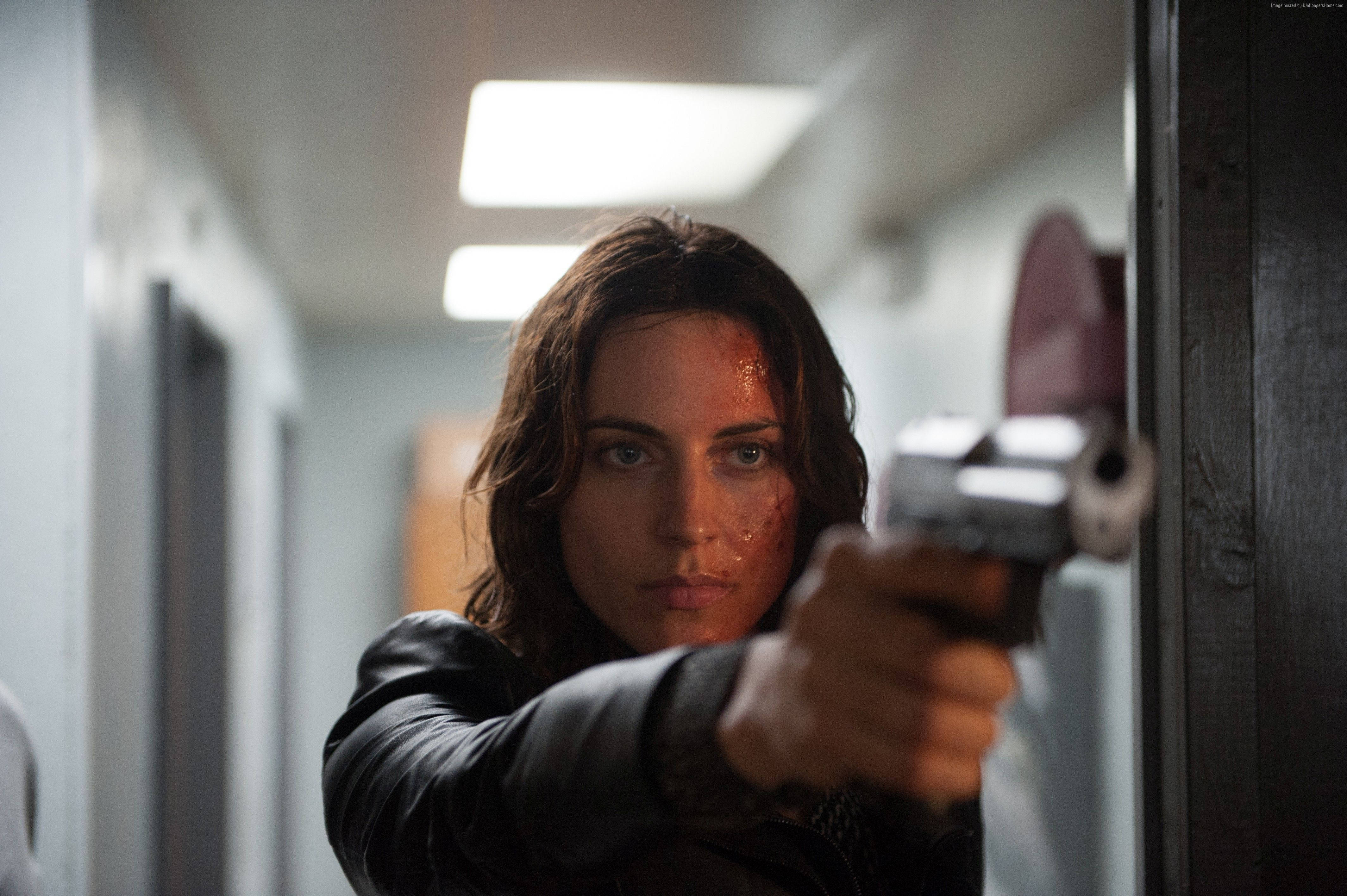 Antje Traue 桌布 壁紙 — 一名滿臉鮮血的女子在昏暗的醫院走廊上，頭頂有螢光燈，用槍瞄準前方。