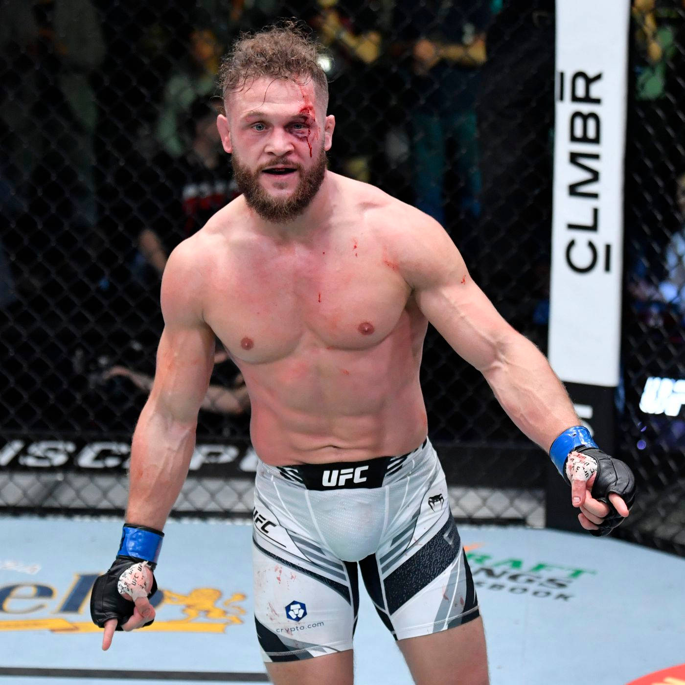 UFC 桌布 壁紙 — 一名滿身鮮血的UFC拳手，眼睛瘀青，短褲破爛，在八角籠內慶祝勝利。