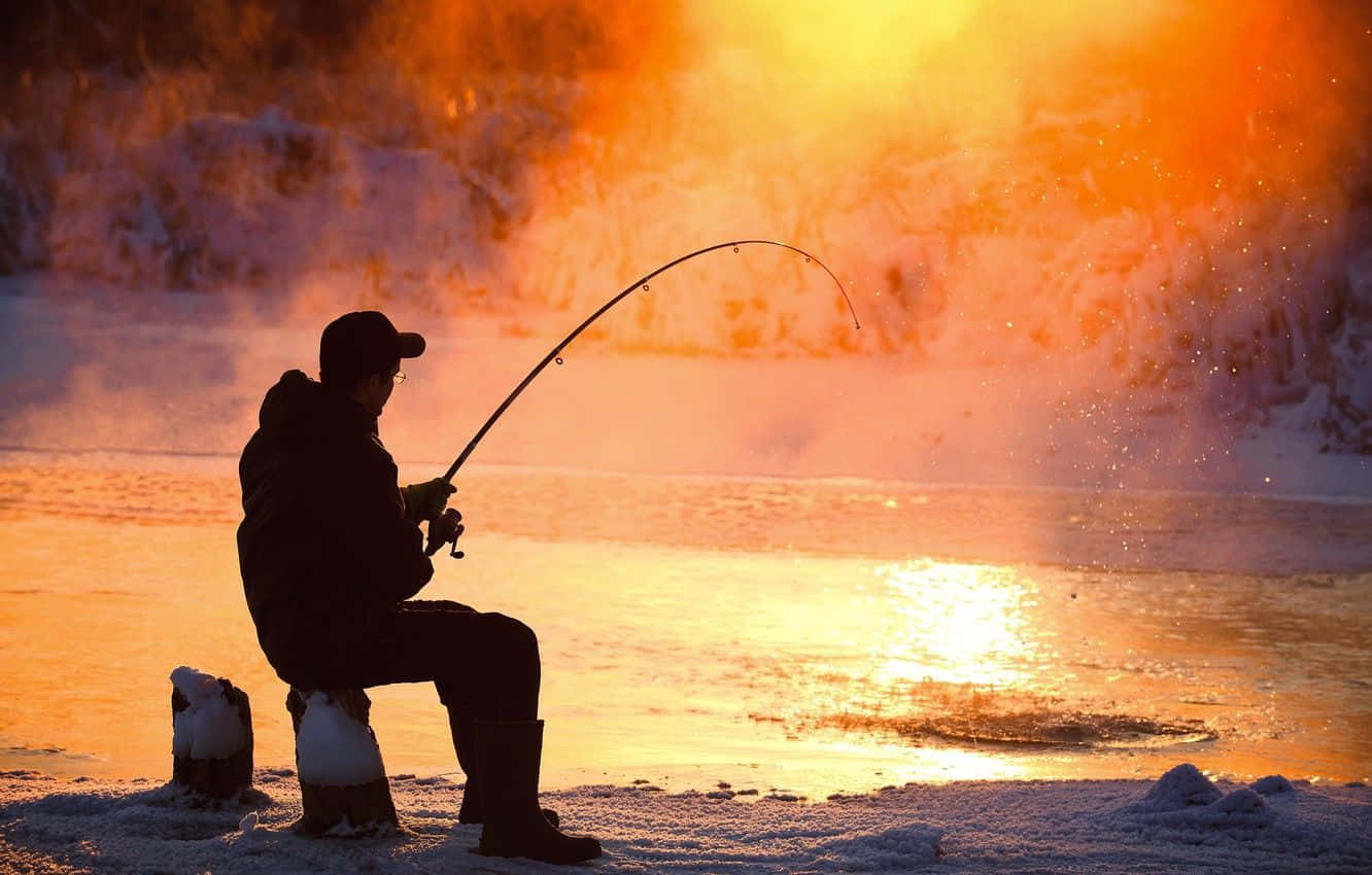 Ice Fishing 桌布 壁紙 — 一名漁夫的剪影在金色日落時分向冒著蒸氣的冬日河流投下釣線。