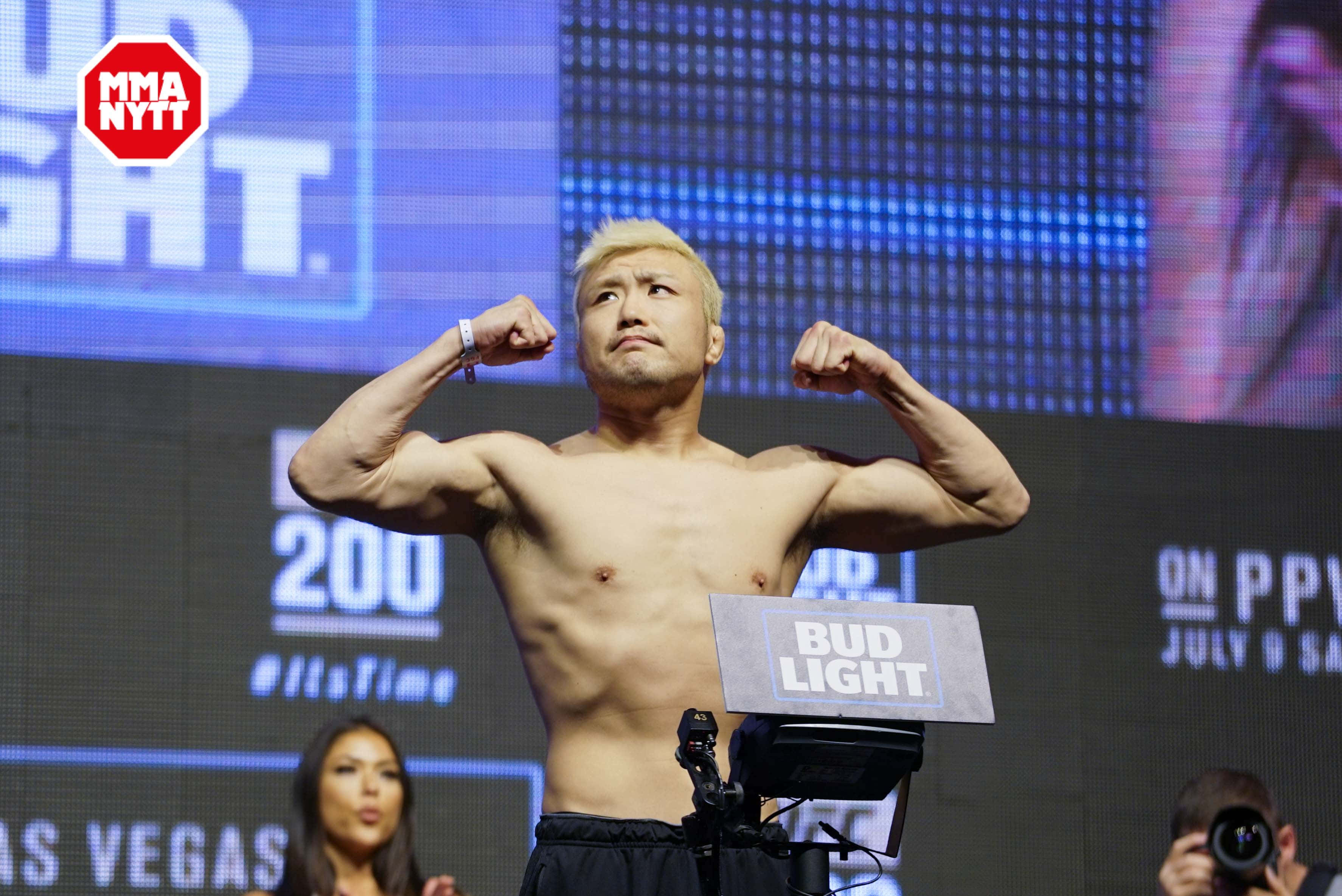 UFC 桌布 壁紙 — 一名漂染金髮的赤裸上身男拳手在明亮的藍色MMA稱重台上，雙臂用力放在體重磅上。