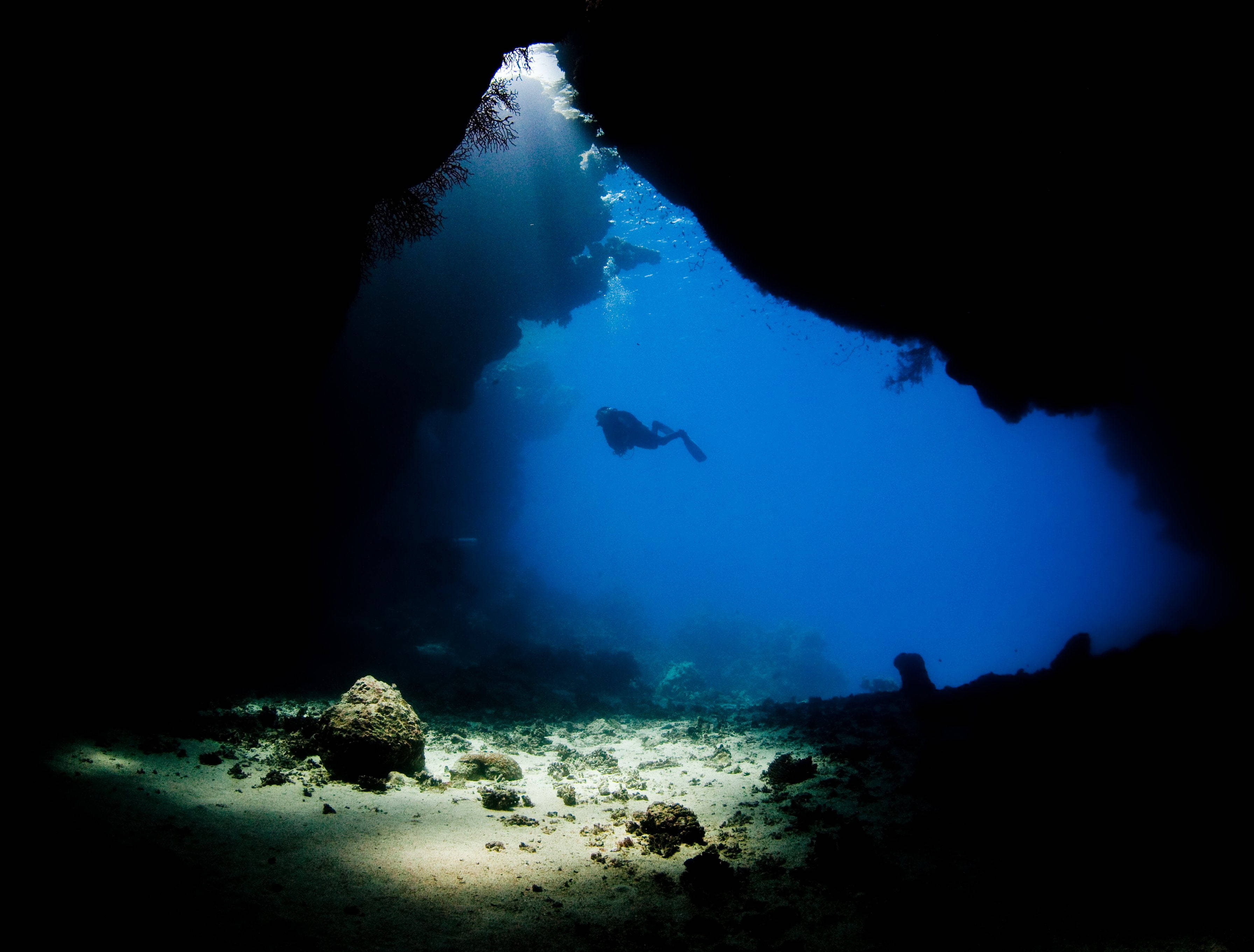 diving 桌布 壁紙 — 一名潛水員在穿過黑暗水下洞穴入口的陽光光束中形成剪影。