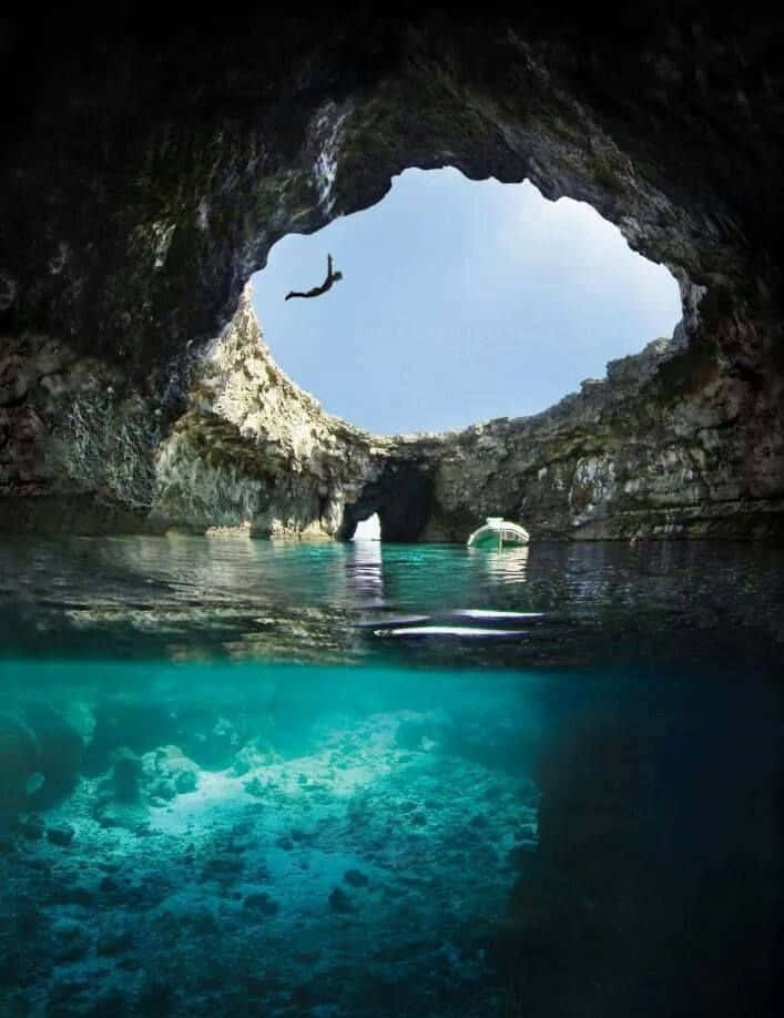 Blue Hole 桌布 壁紙 — 一名潛水員從天然海蝕洞的開口跳入清澈碧綠的海水中，朝向明亮的藍天。