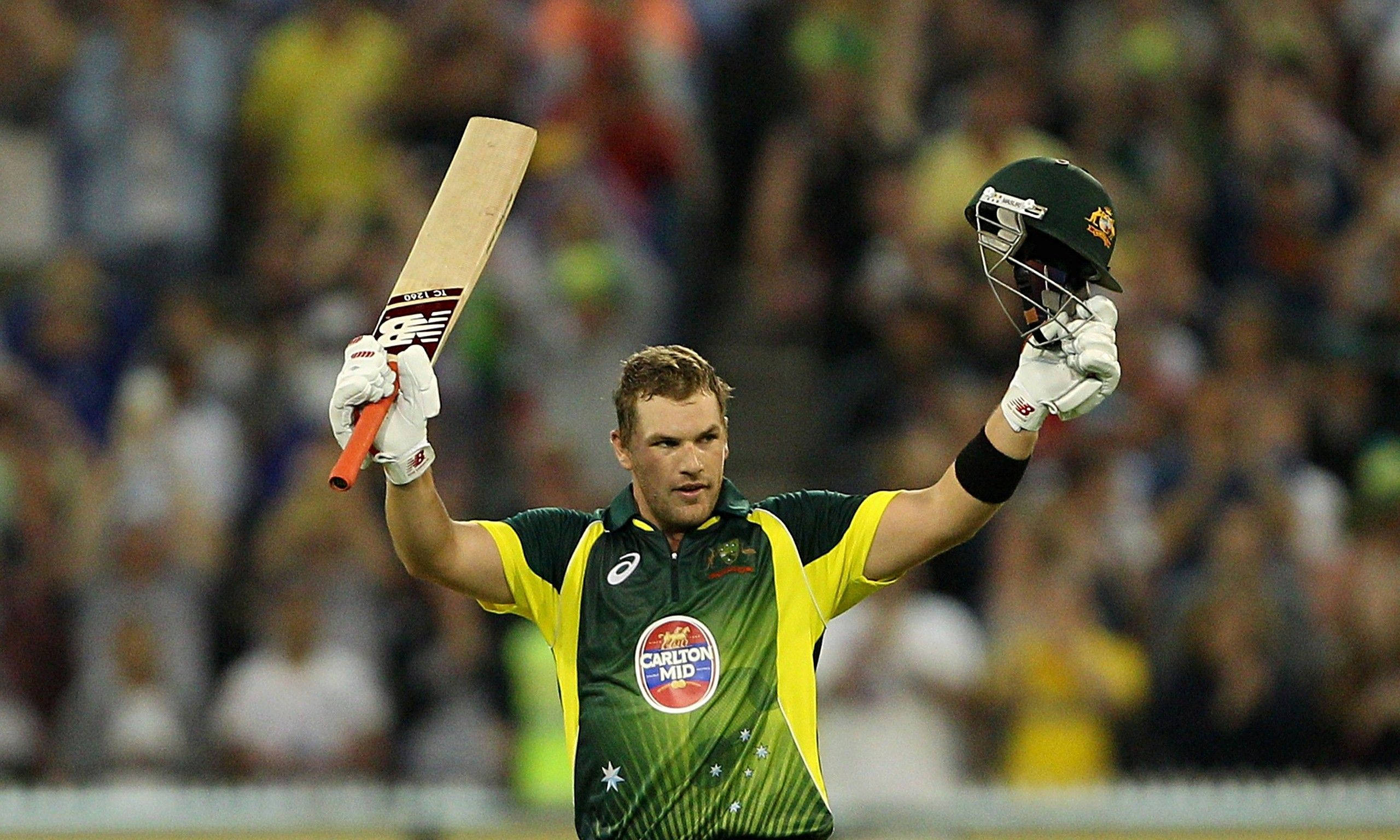 Aaron Finch 桌布 壁紙 — 一名澳洲板球運動員在體育場燈光下高舉球棒和頭盔，勝利慶祝。