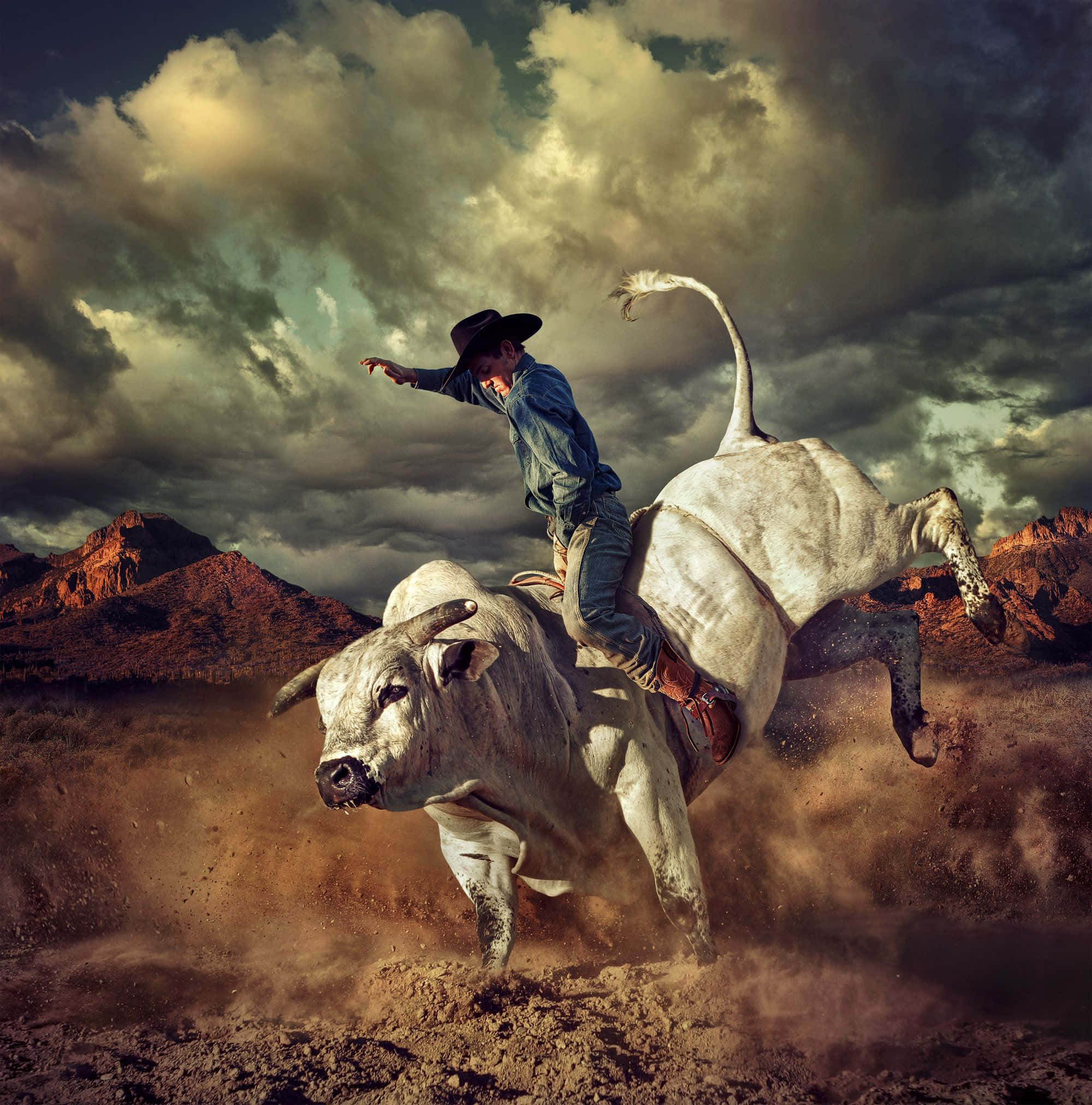 Bull Rider 桌布 壁紙 — 一名牛仔在戲劇性的多雲天空下，背景有紅色岩石山，緊緊抓住一隻跳躍的白色公牛。