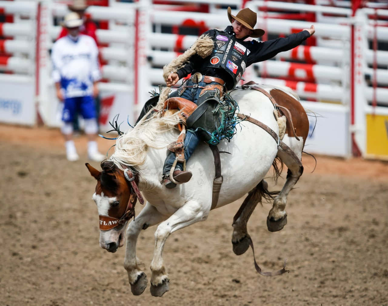 Rodeo 桌布 壁紙 — 一名牛仔在泥地競技場的牛仔競技活動中，緊緊抓住一匹正在尥蹶子的白棕色馬。