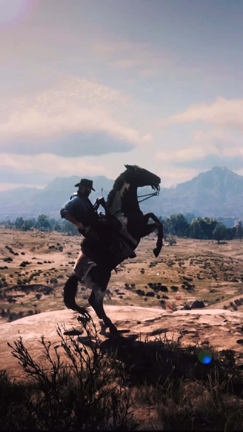Cowboy 桌布 壁紙 — 一名牛仔騎著一匹後腿站立的馬，在岩石山頂上，以廣闊的山脈地平線為背景，天空明亮。