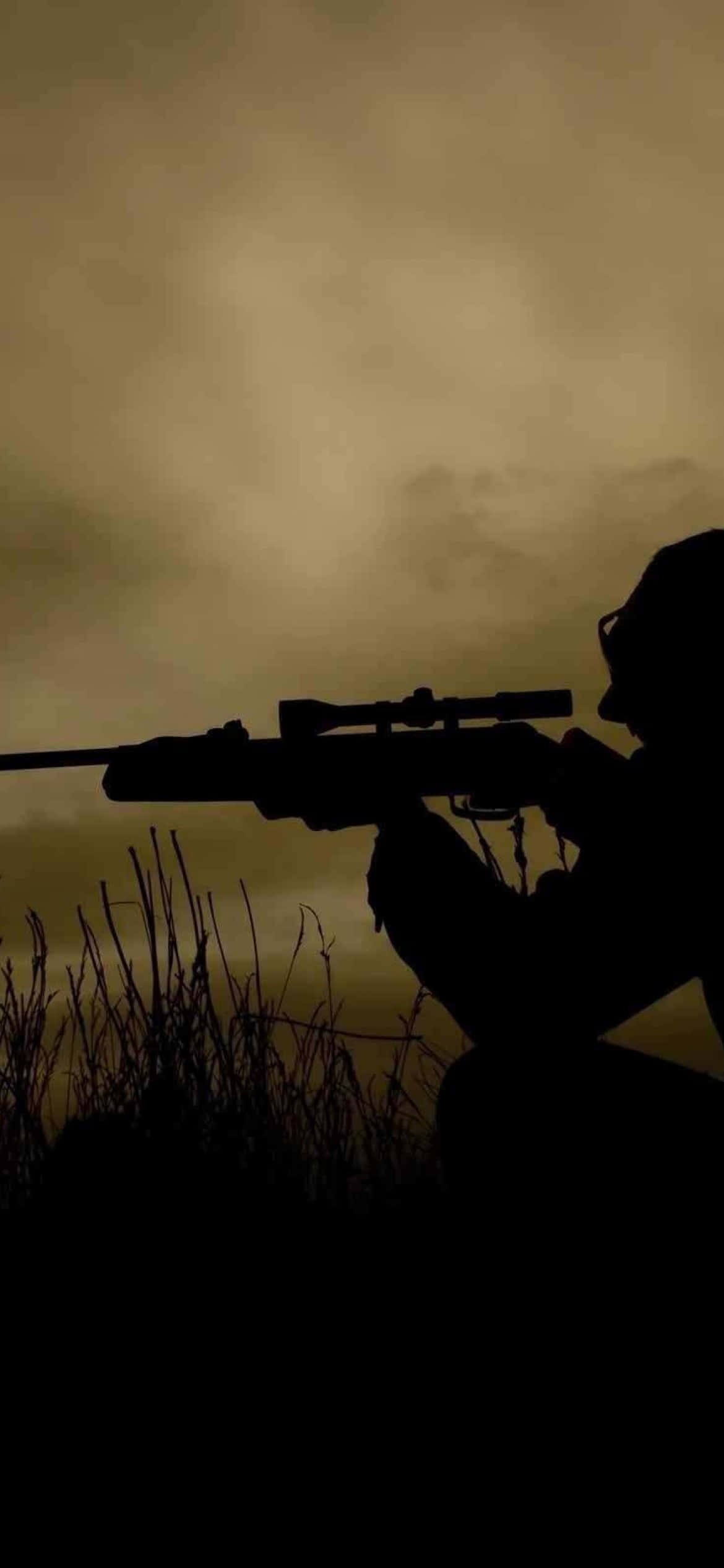 hunter hunter 桌布 壁紙 — 一名狙擊手蹲伏在高草叢中，瞄準步槍，背景是朦朧的金色天空的剪影。