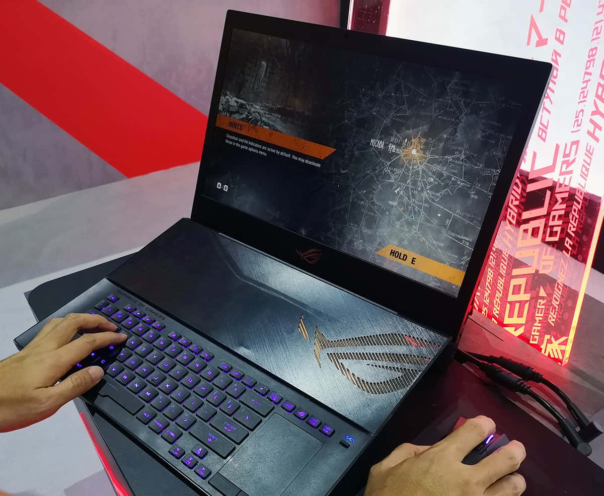 華碩 ROG 桌布 壁紙 — 一名玩家在黑色ASUS ROG筆記型電腦上玩戰術射擊遊戲，配有發光紫色按鍵和滑鼠，位於紅白品牌攤位。