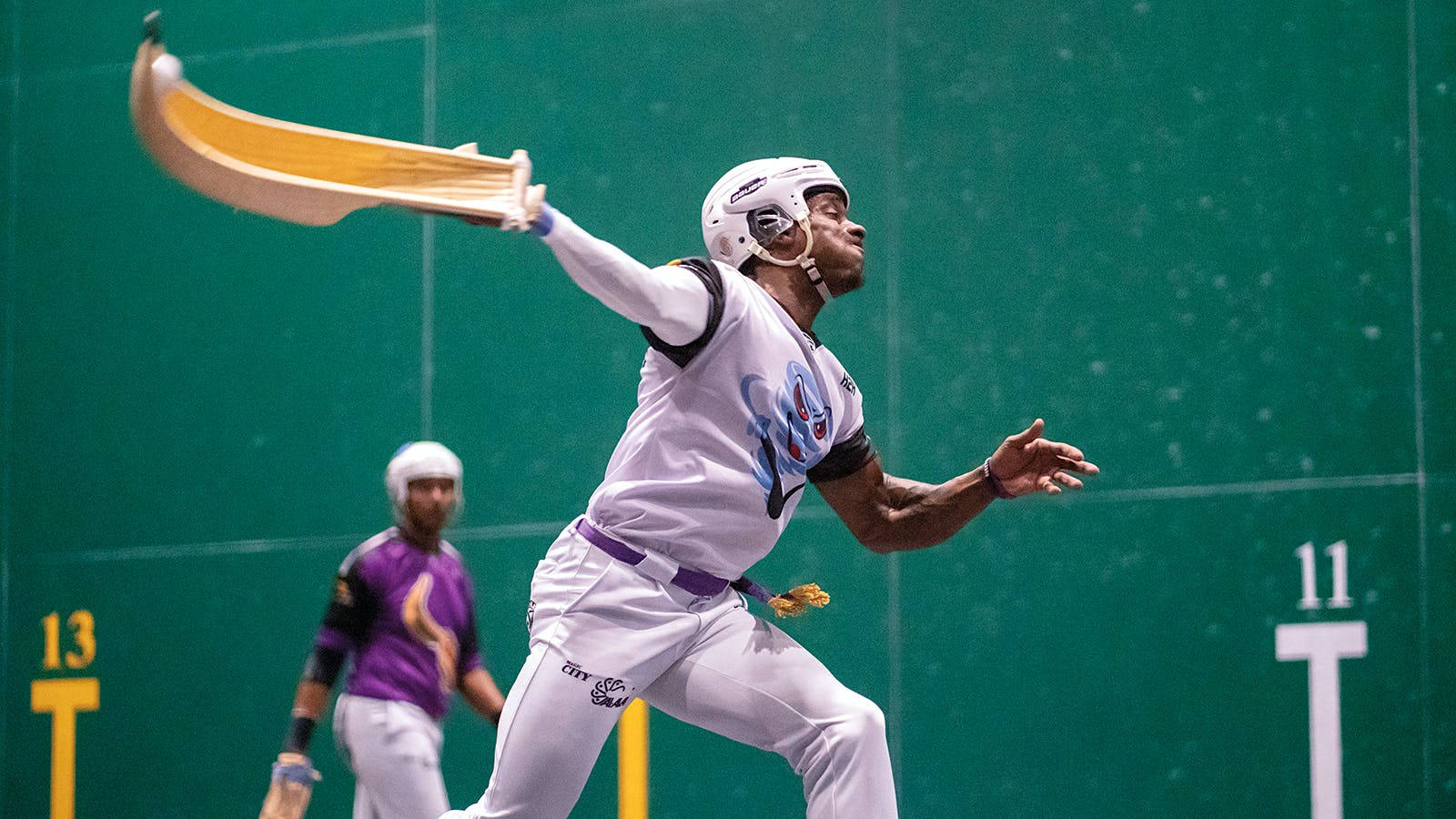 Jai Alai 桌布 壁紙 — 一名球員在綠色牆壁的球場內，於一場競爭激烈的回力球比賽中，專注地揮動彎曲球拍。
