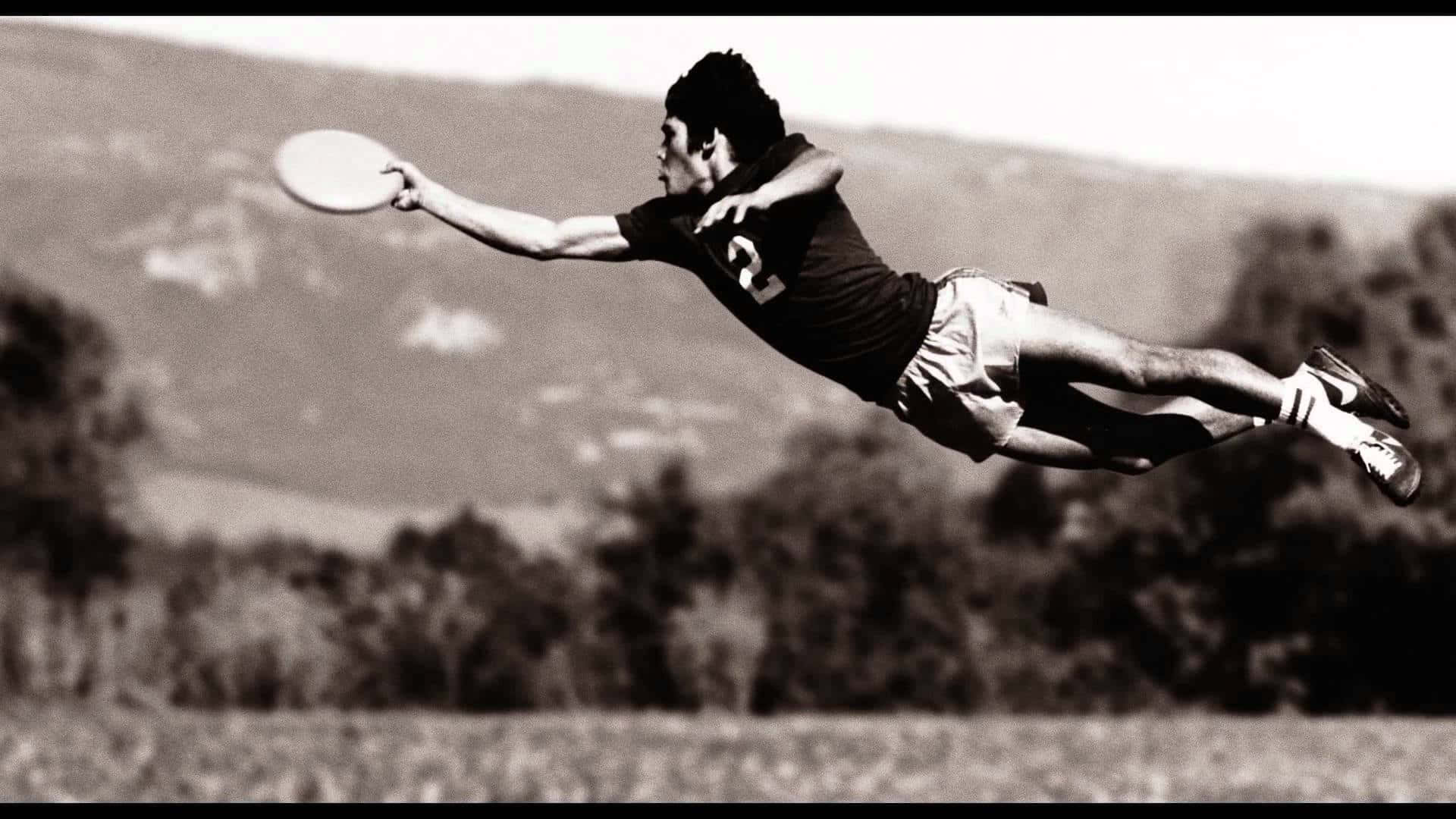 Frisbee 桌布 壁紙 — 一名男子以黑白畫面在空中跳躍，接住飛盤，背景是朦朧的山巒。