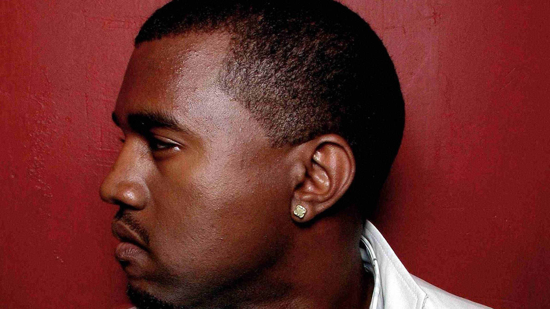 Kanye 桌布 壁紙 — 一名男子側面輪廓，背景為有紋理的紅牆，身穿白襯衫，戴著金耳環。