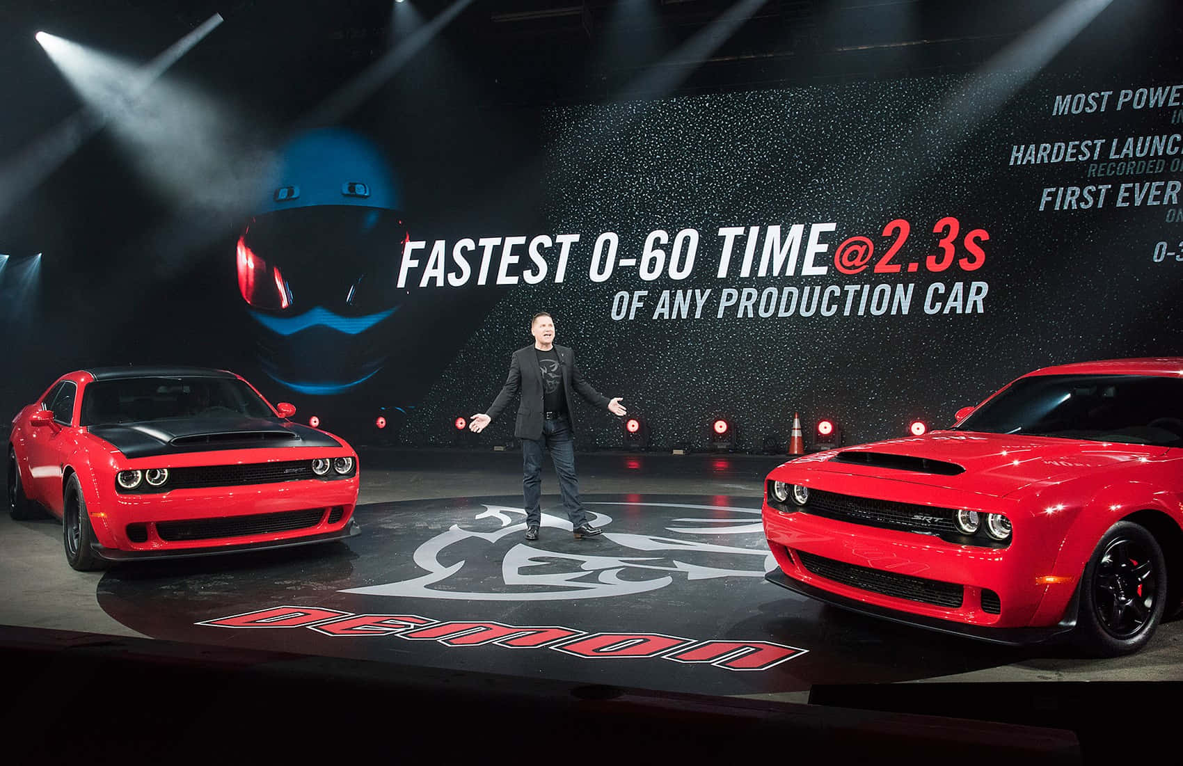 Dodge 桌布 壁紙 — 一名男子勝利地站在兩輛紅色道奇惡魔超級跑車之間，在戲劇性的舞台燈光下，星空背景宣告最快的0-60時間。