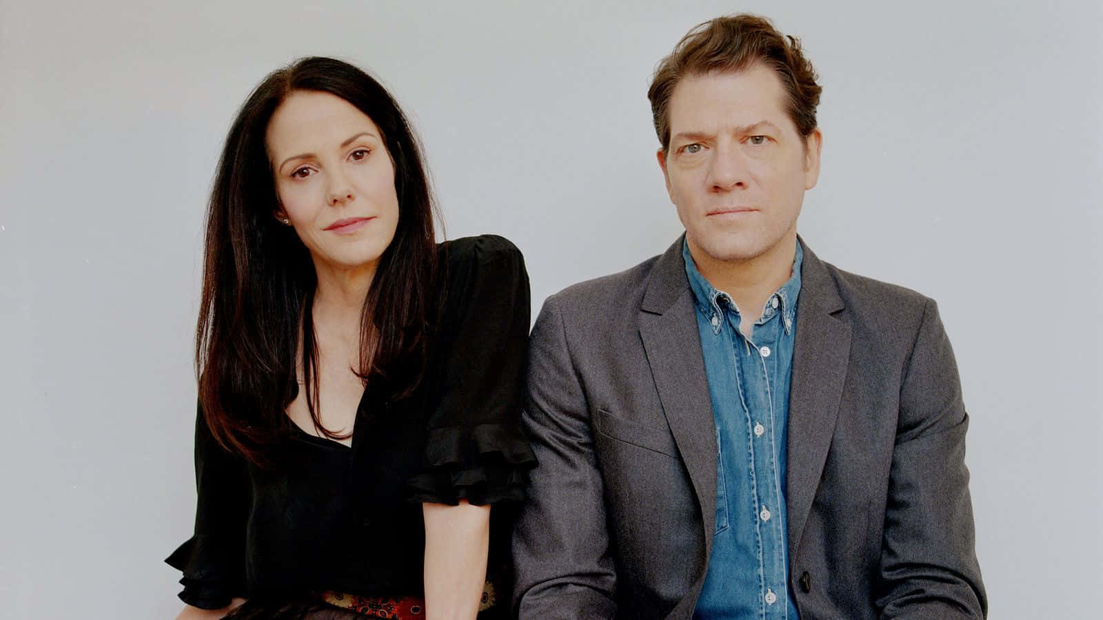 mary louise parker 桌布 壁紙 — 一名男子和一名女子並排坐在純淺灰色背景前，兩人都以中性表情直視鏡頭。