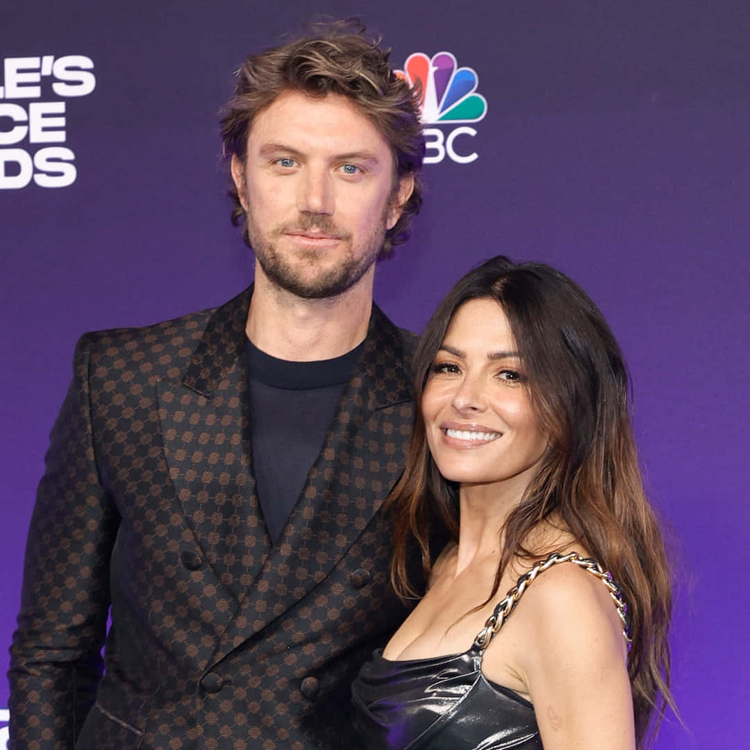 sarah shahi 桌布 壁紙 — 一名男子和一名女子在人民選擇獎的紫色地毯上一起擺姿勢，背後有NBC品牌標誌。