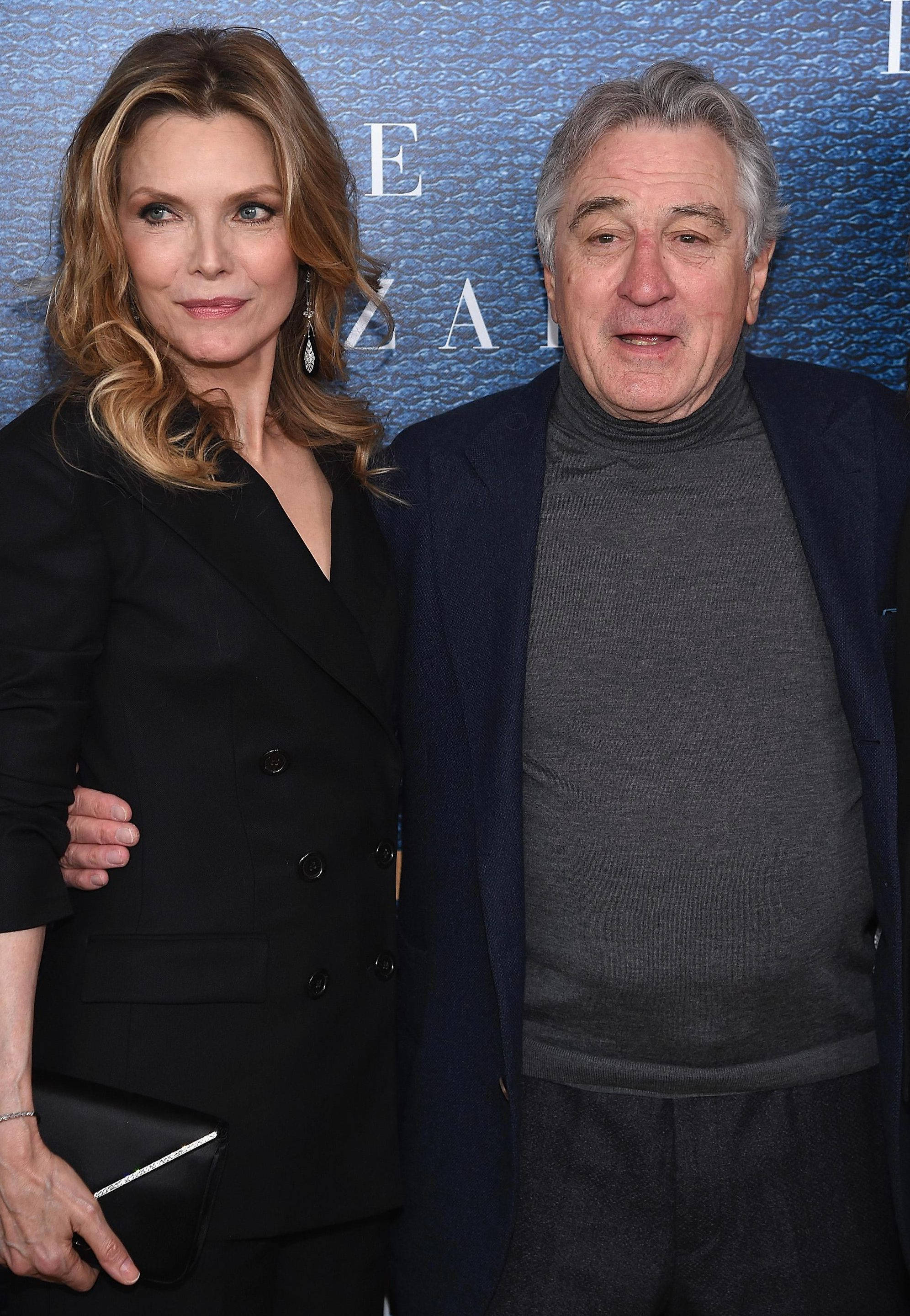 Robert De Niro 桌布 壁紙 — 一名男子和一名女子在正式活動中，在帶有部分文字的紋理藍色背景前一起擺姿勢。