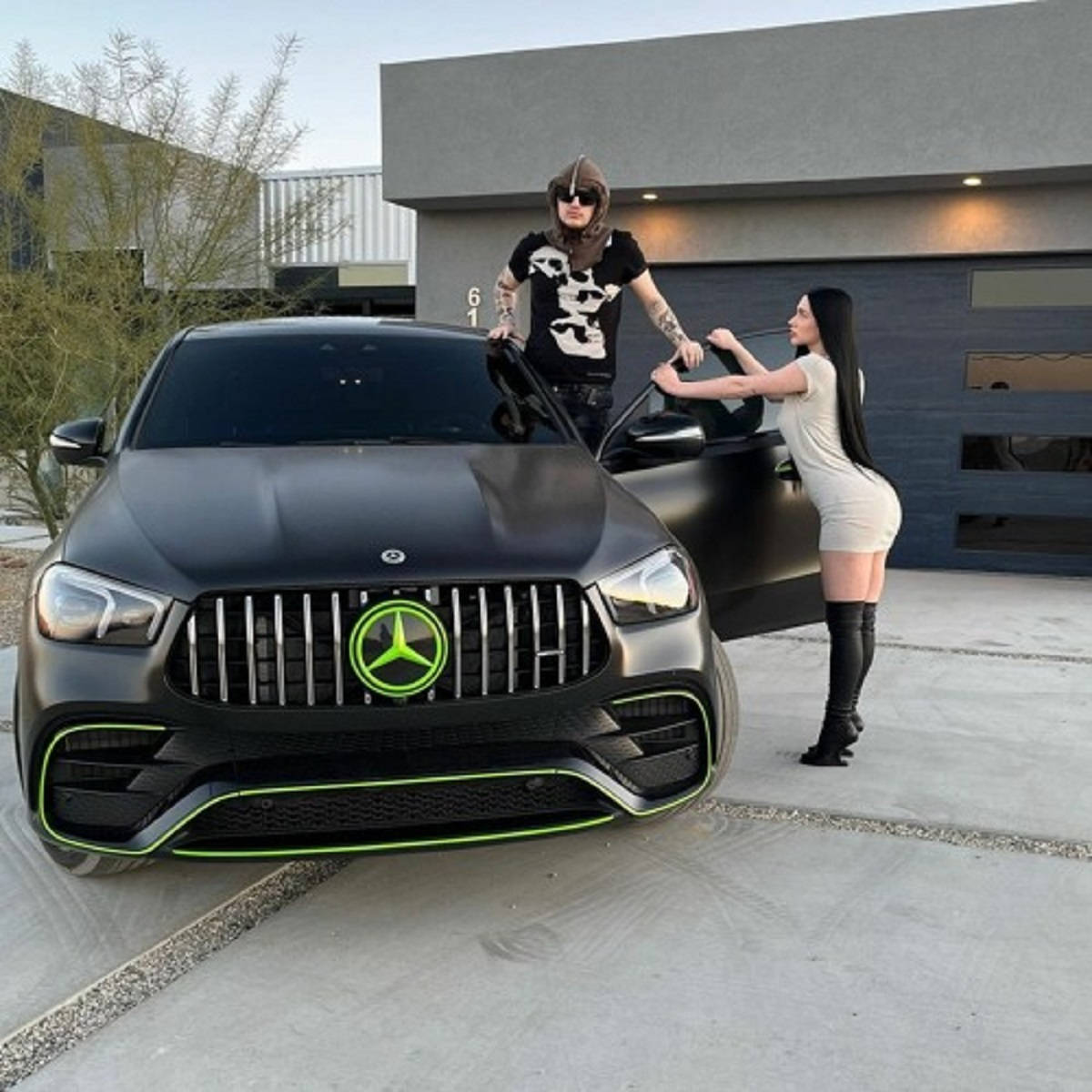 Mercedes 桌布 壁紙 — 一名男子和一名女子在現代房屋前，在一輛帶有發光綠色裝飾的啞光黑色梅賽德斯AMG旁擺姿勢。