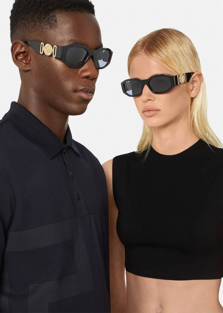 Sunglasses 桌布 壁紙 — 一名男子和一名女子在純白色背景前佩戴帶有金色標誌的醒目黑色太陽眼鏡。